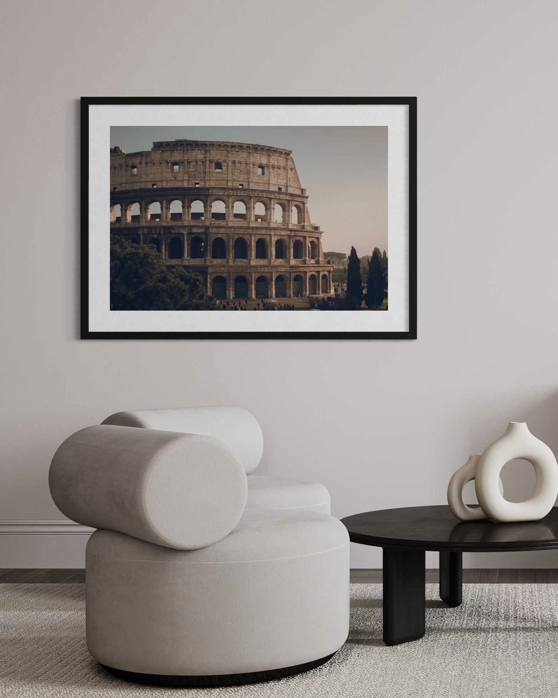 Framed photograph of the Colosseum on a wall above a modern chair and table.