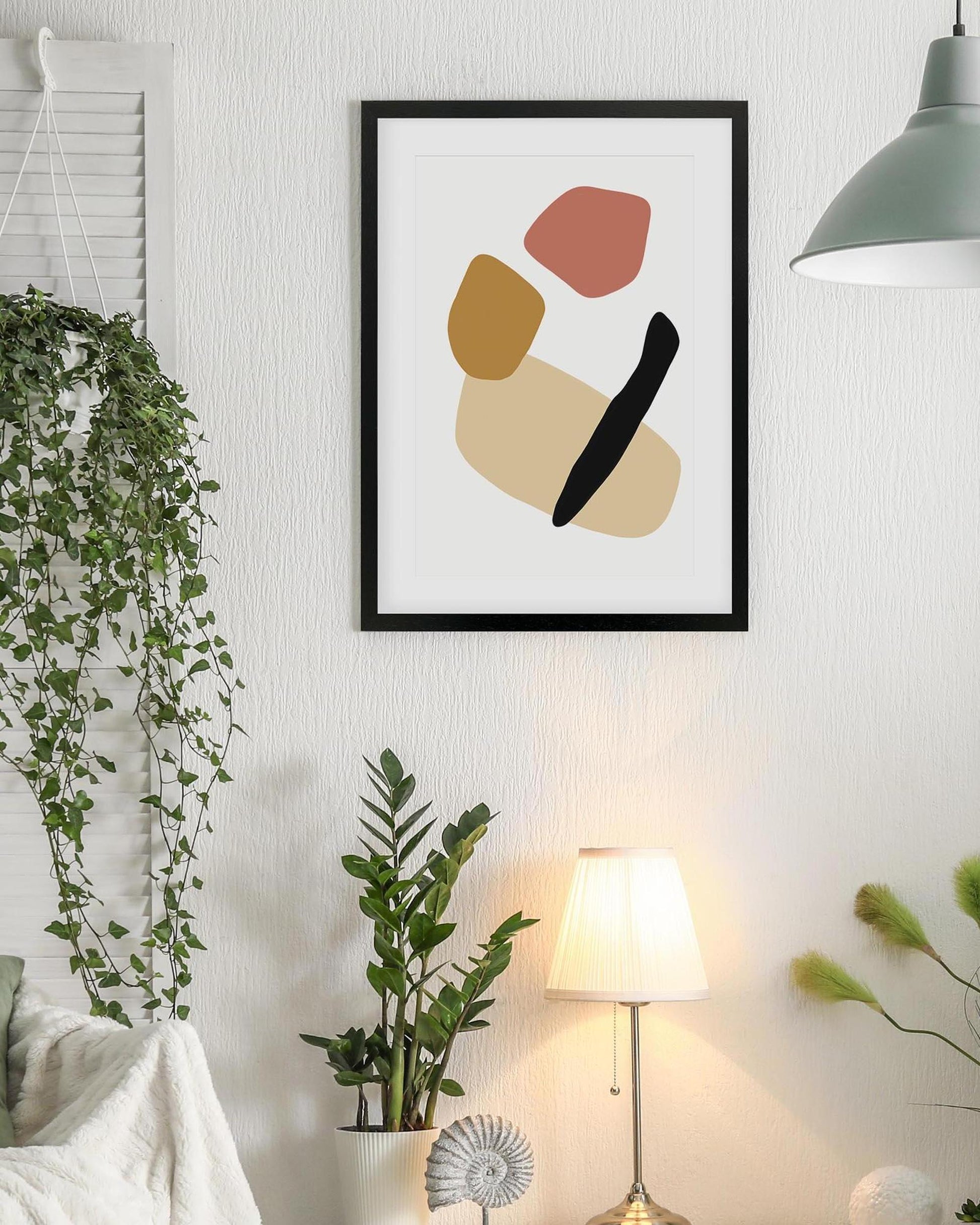 Framed abstract art piece on a wall with plants and a lamp in the foreground
