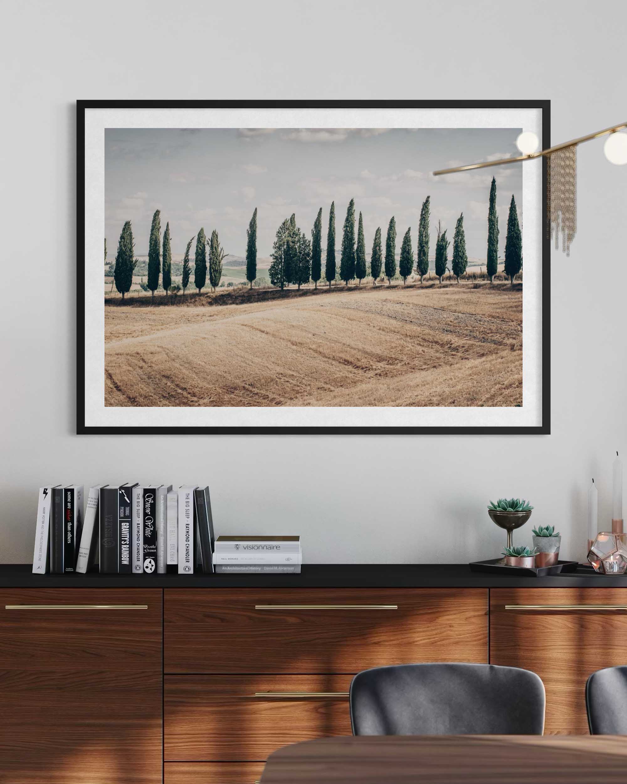 Framed landscape print of a field with trees on a wall above a desk.
