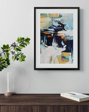 Framed abstract painting on a wall above a wooden surface with a candle and book.