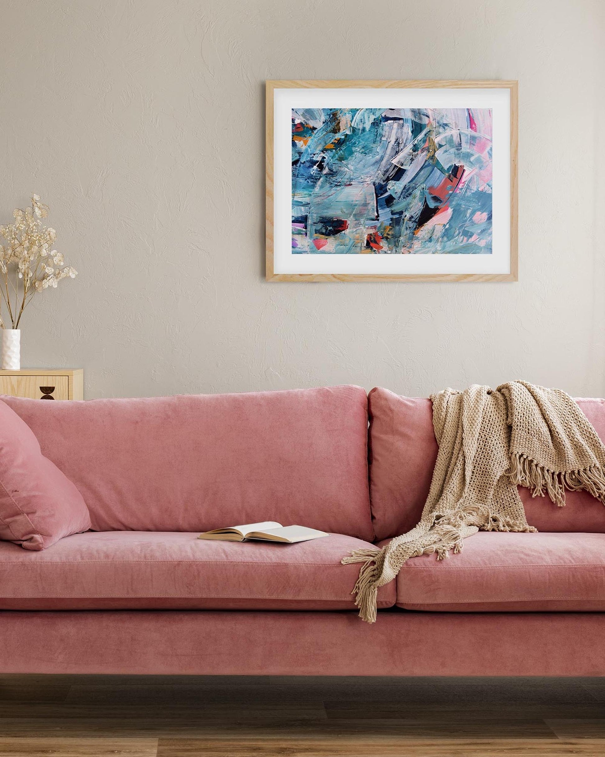 Pink sofa with a blanket and book in a living room with abstract art on the wall.