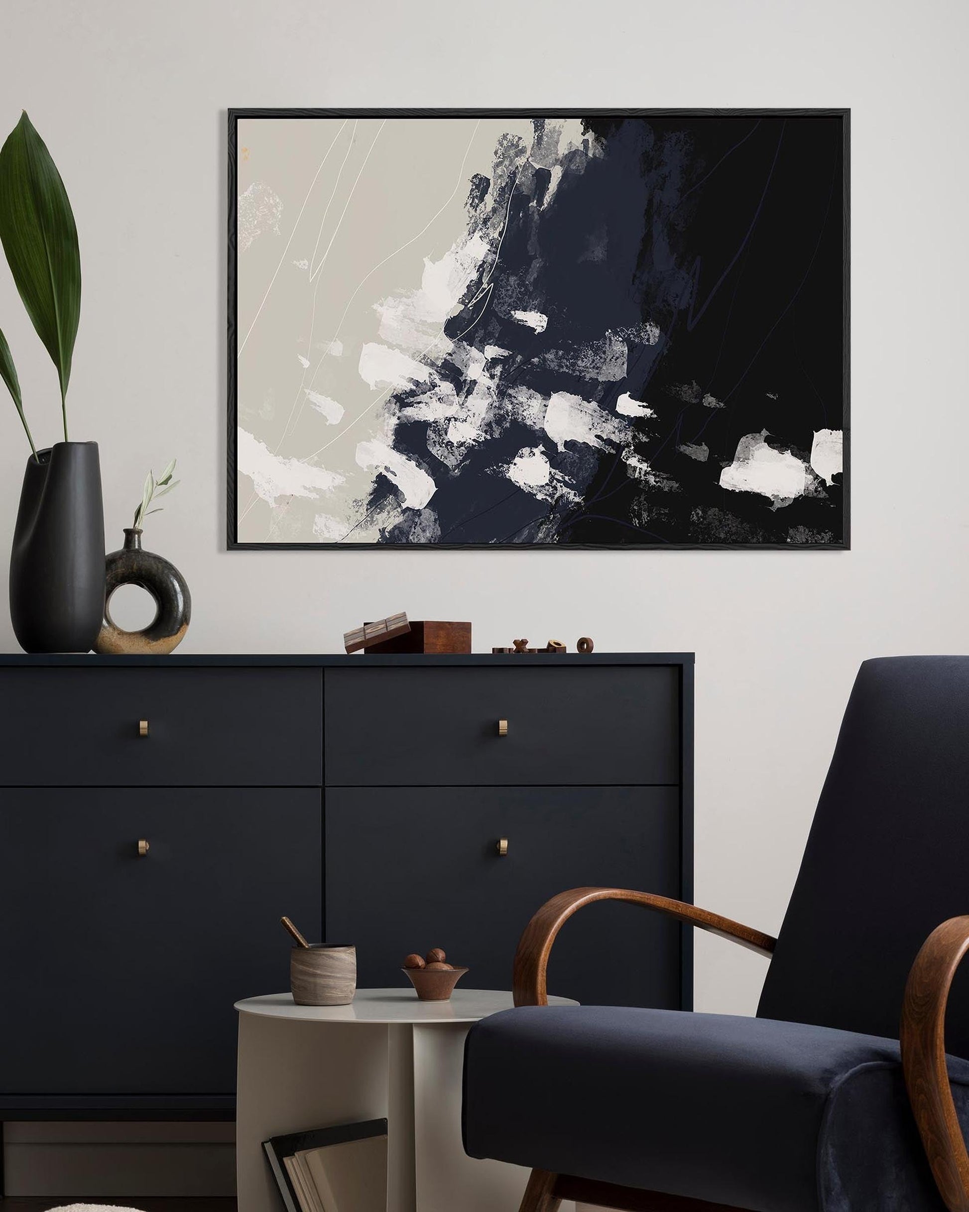Abstract art piece on a wall above a black dresser with a chair and small table.