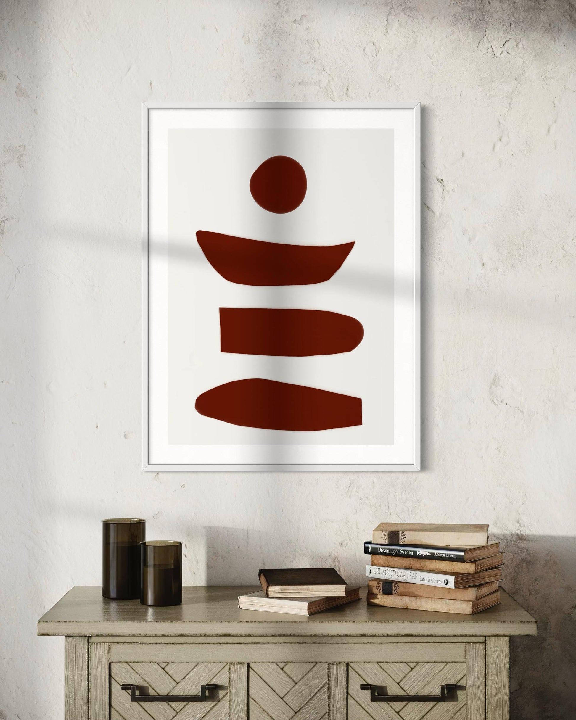 Framed abstract art piece with brown shapes on a white wall above a wooden cabinet.