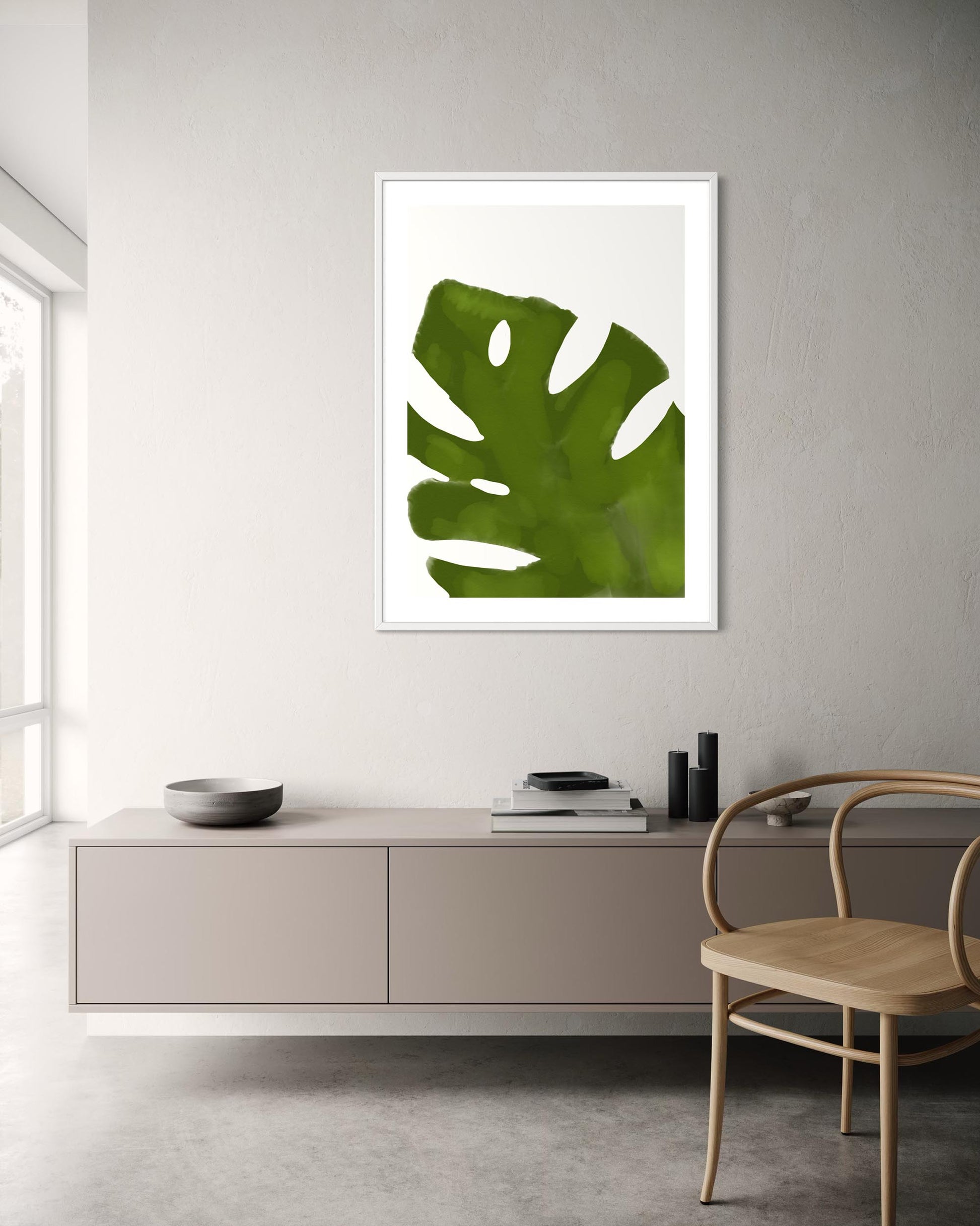 Framed green leaf print on a wall in a modern room with a cabinet and chair.