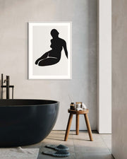 Framed black silhouette art print of a woman sitting on a wall in a modern bathroom.