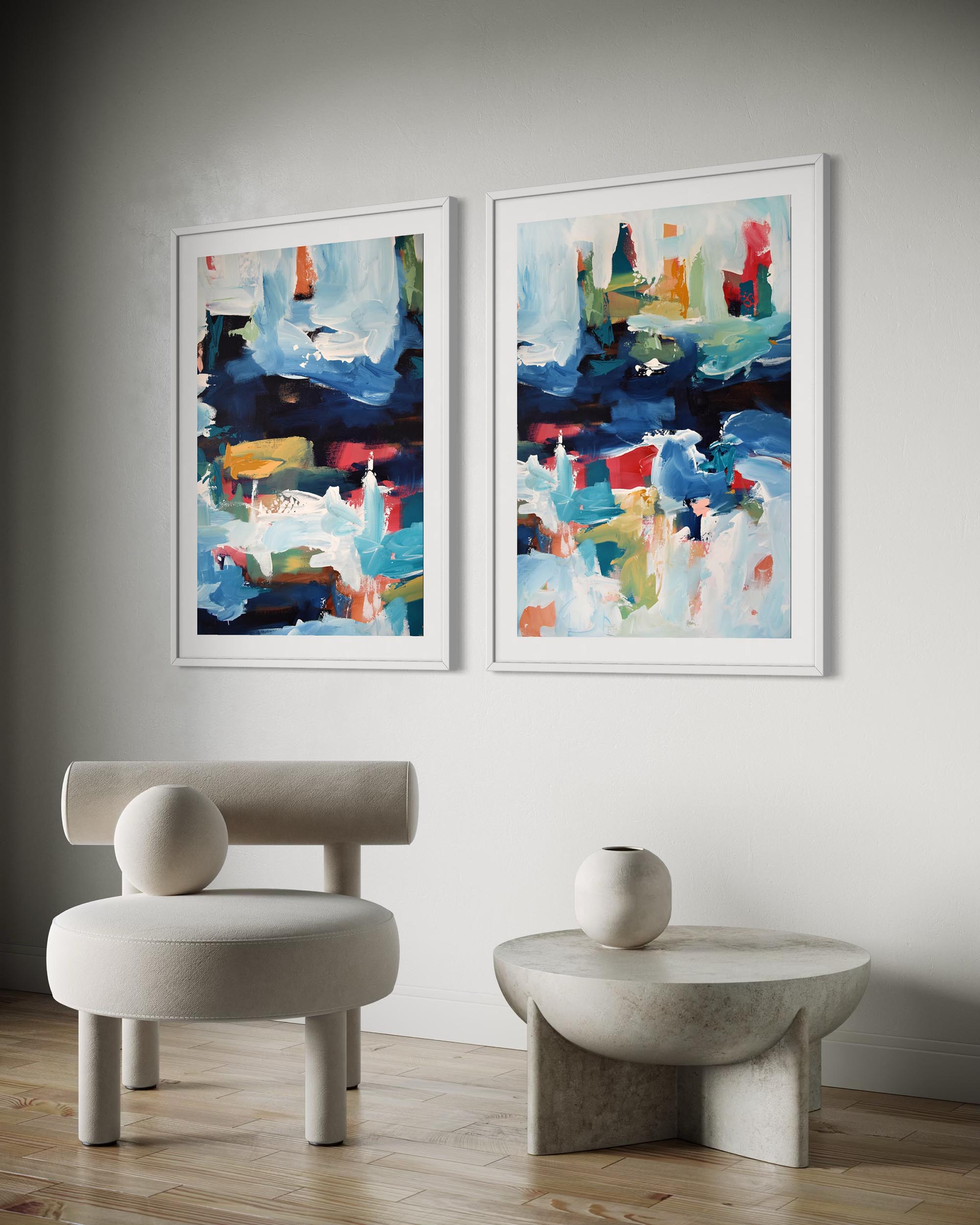 Two abstract paintings on a wall with a modern chair and table below.