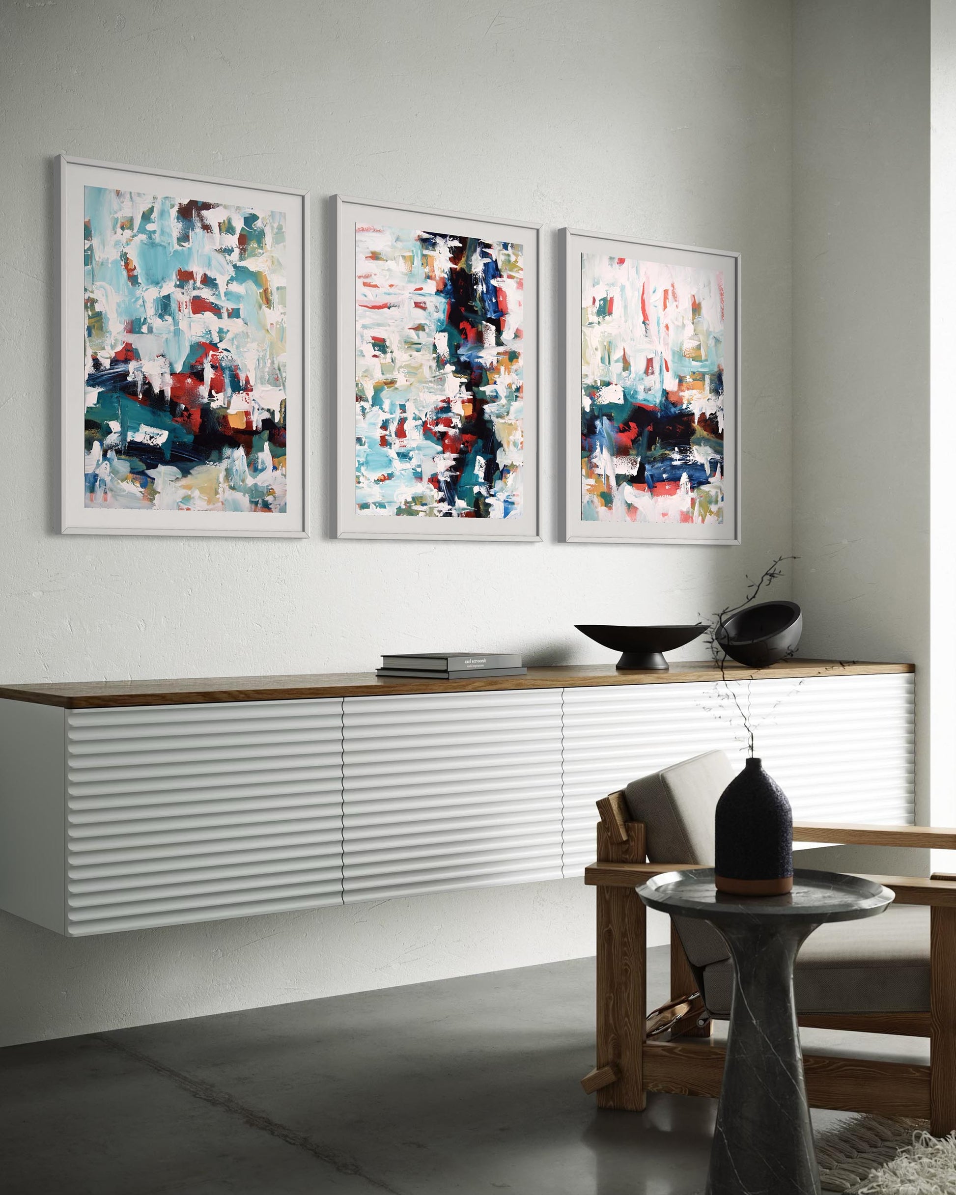 Three abstract paintings on a wall above a console table in a modern living room.