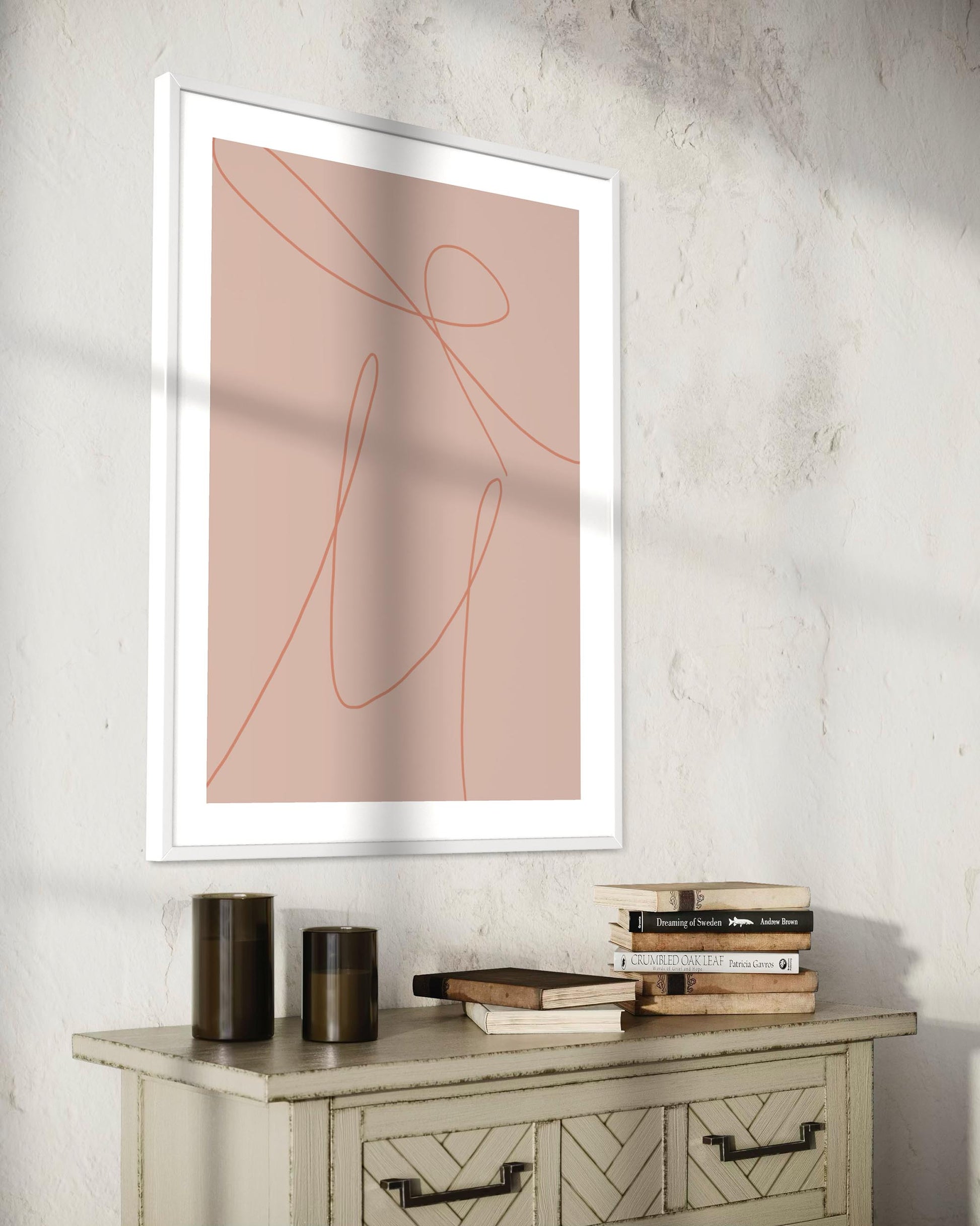 Framed abstract art on a wall above a wooden console table with books and candles.
