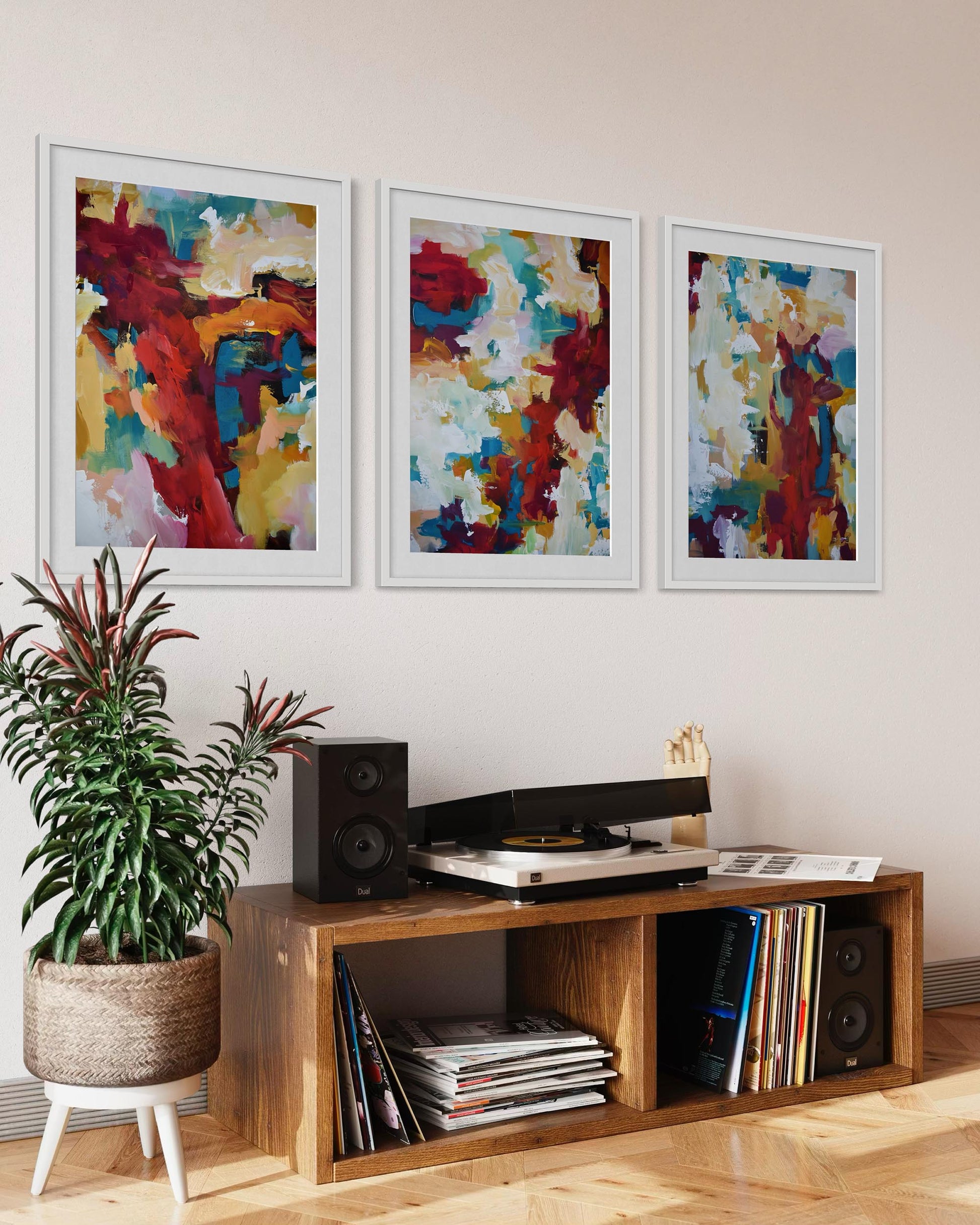 Wooden entertainment console with records, speakers, and a plant in a room with abstract art on the wall.