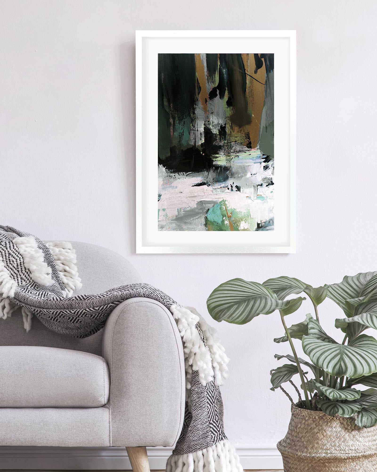 Framed abstract art print on a wall above a sofa with a plant in the foreground.