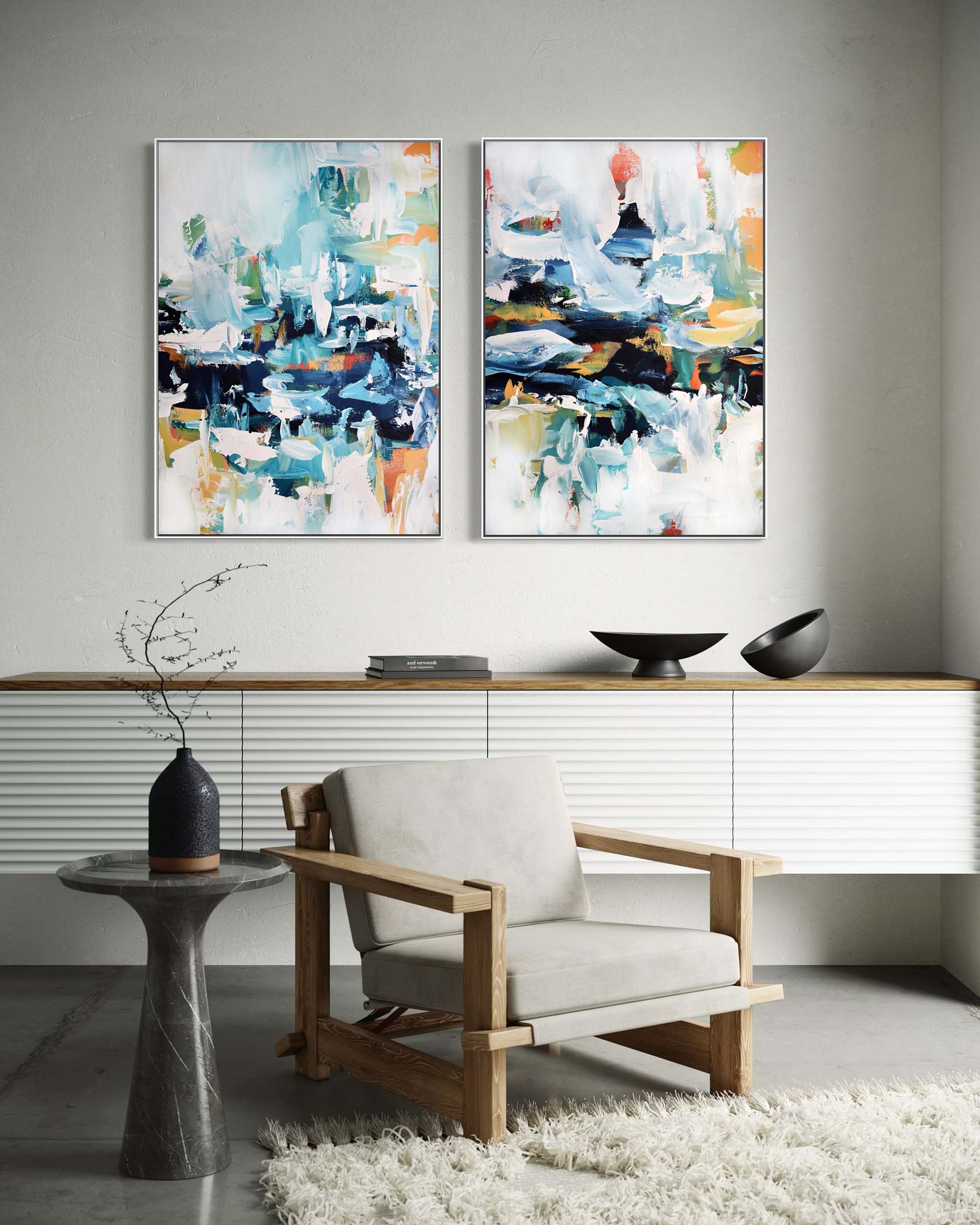 Two abstract paintings on a wall above a modern chair and side table.
