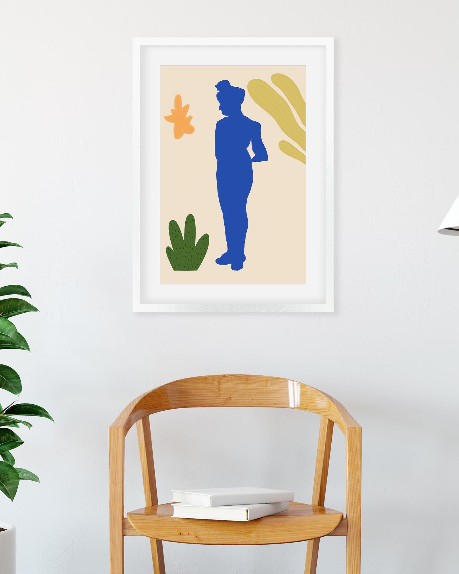 Framed abstract art print with a blue silhouette and colorful shapes on a white wall above a wooden chair.
