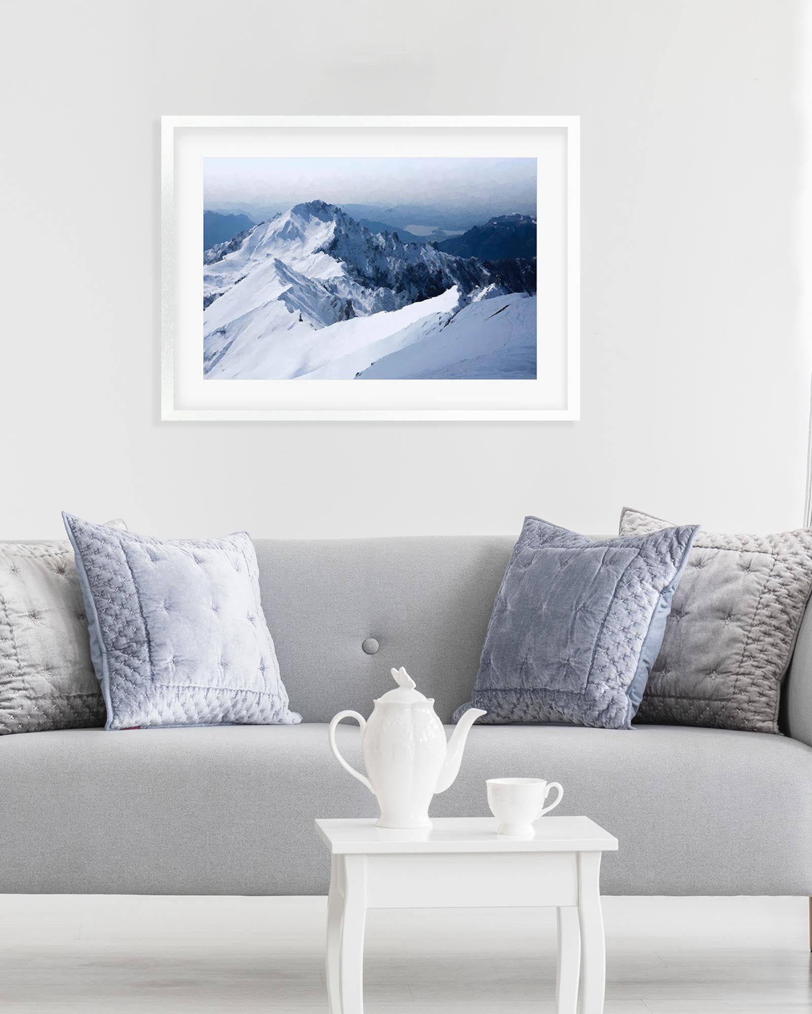Framed mountain landscape print on a wall above a gray sofa with decorative pillows.