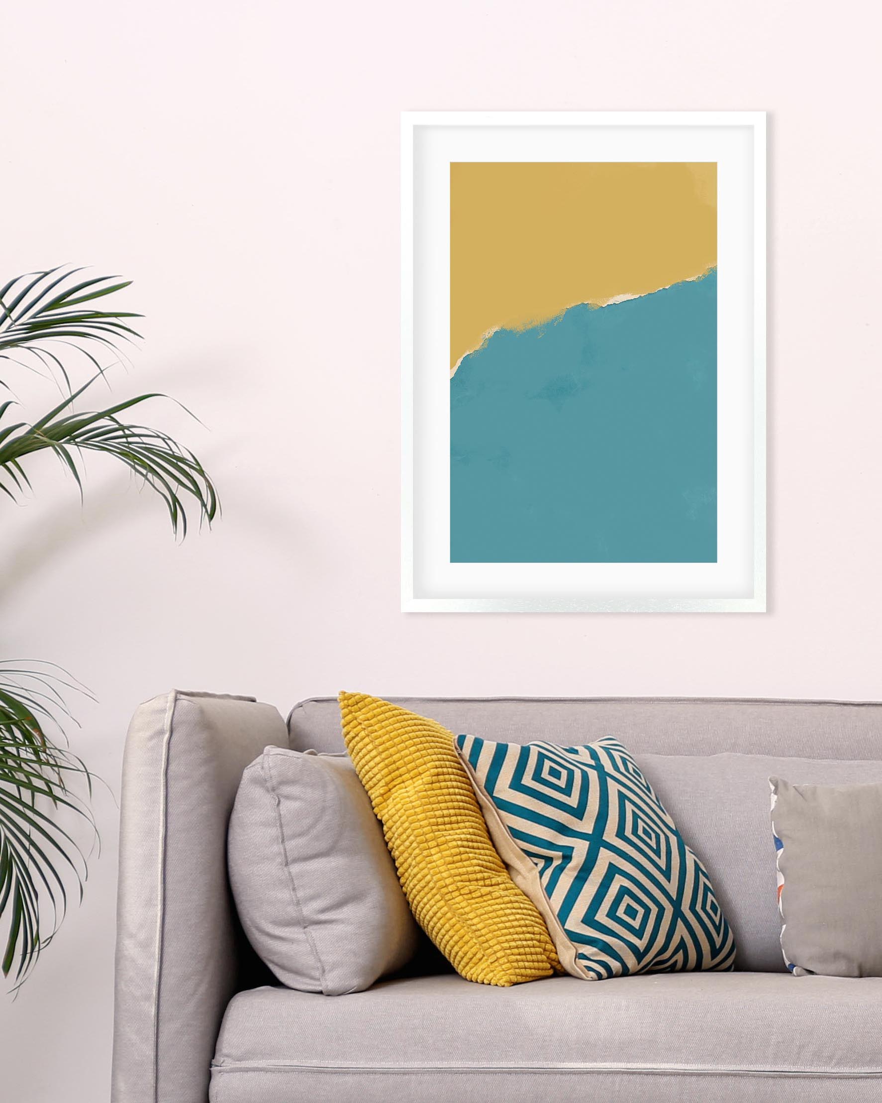 Framed abstract art print with yellow and blue colors above a sofa with patterned cushions.