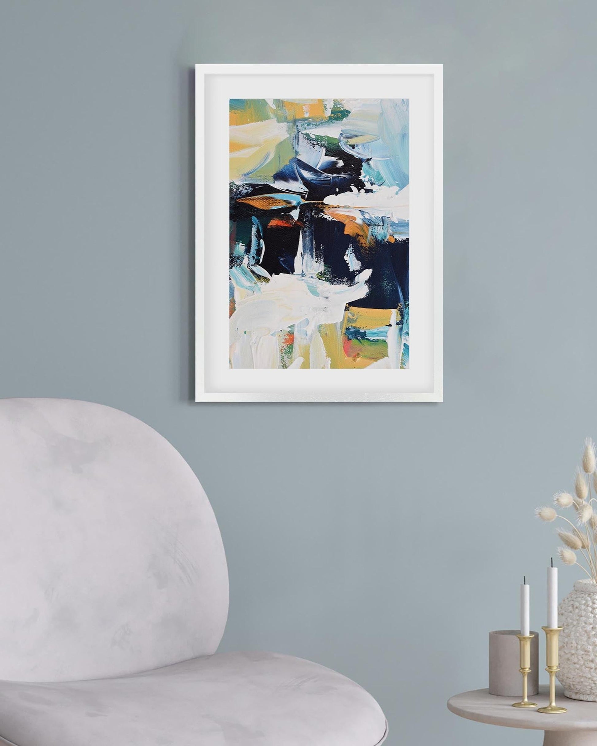 Framed abstract art on a wall above a chair and side table with decorative items.