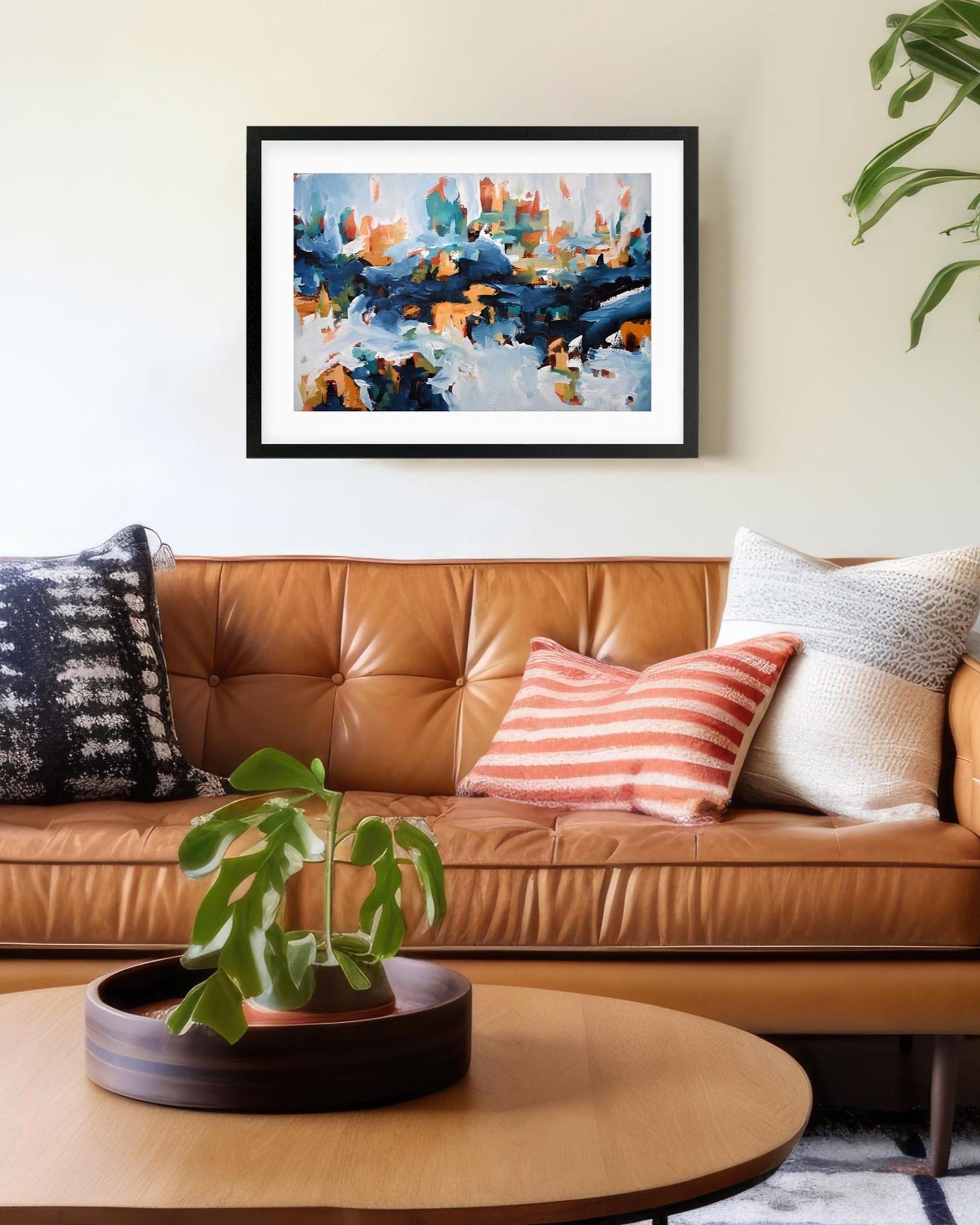Living room with a brown leather sofa, decorative pillows, and a framed abstract painting on the wall.
