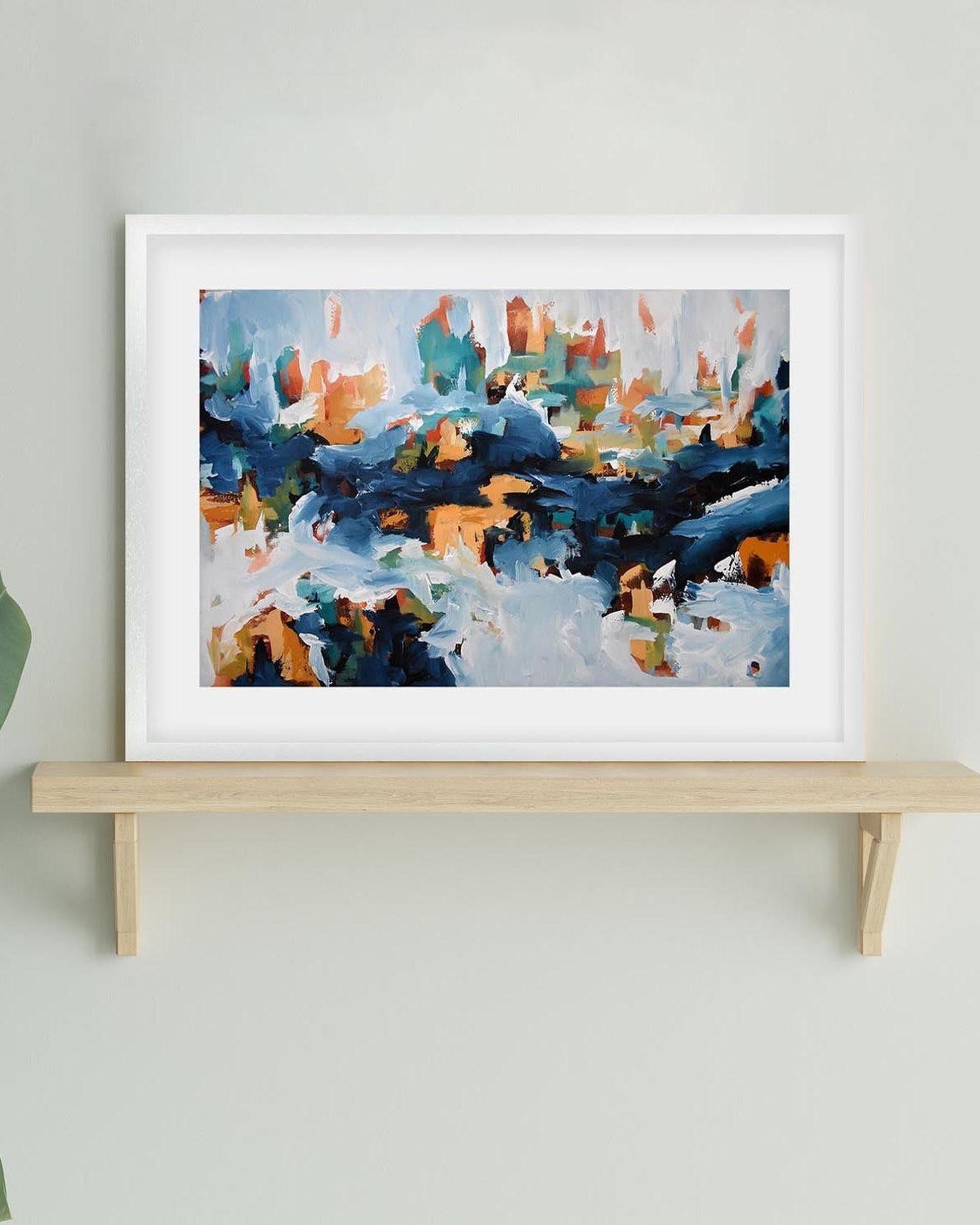 Framed abstract painting on a wooden shelf against a light gray wall