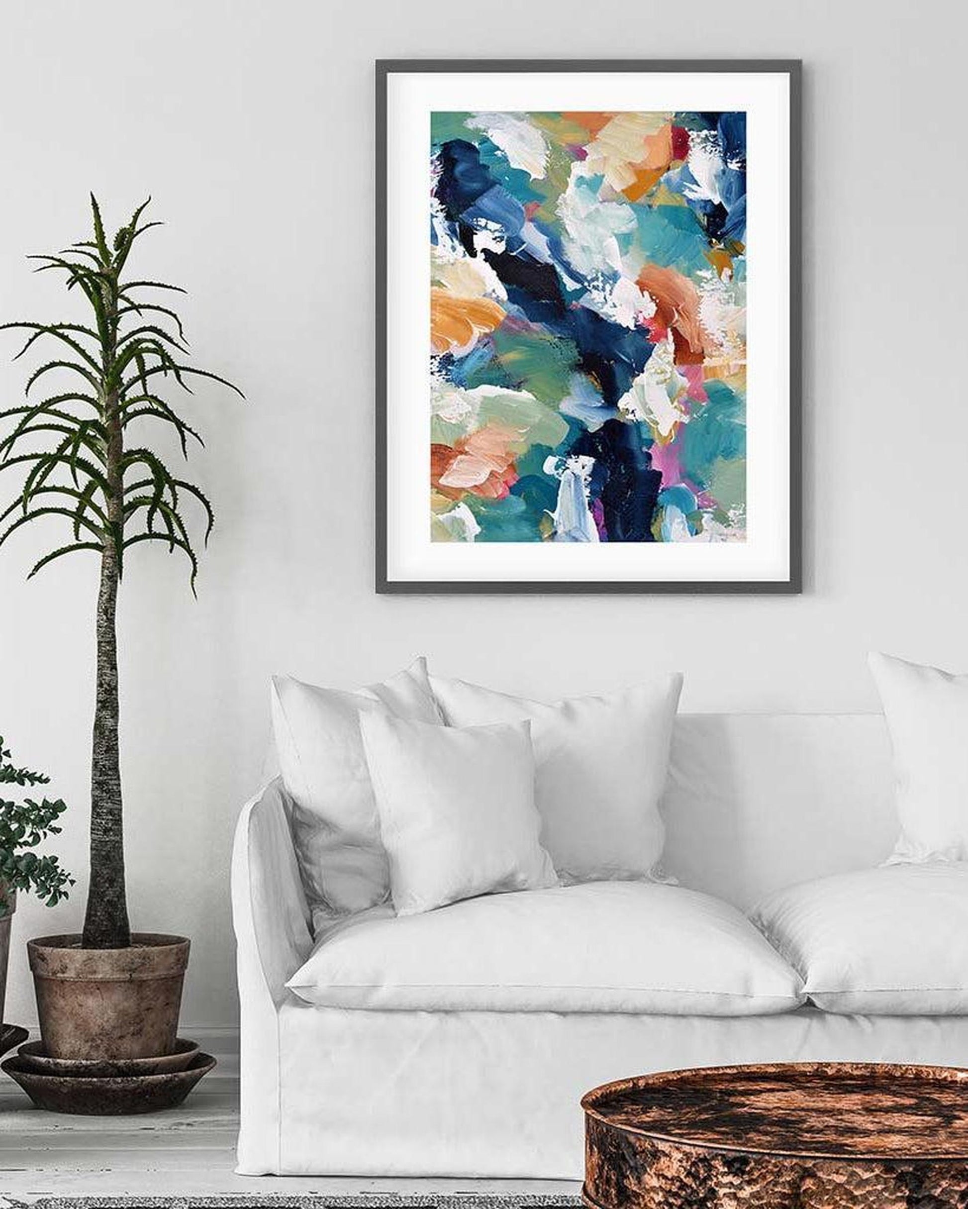Framed abstract art print on a wall above a white sofa with decorative pillows.