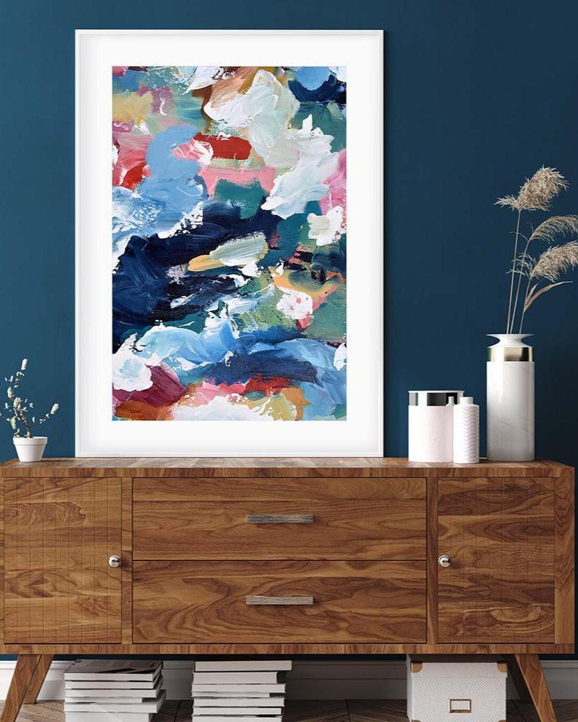 Colorful abstract art print on a wooden sideboard against a blue wall.