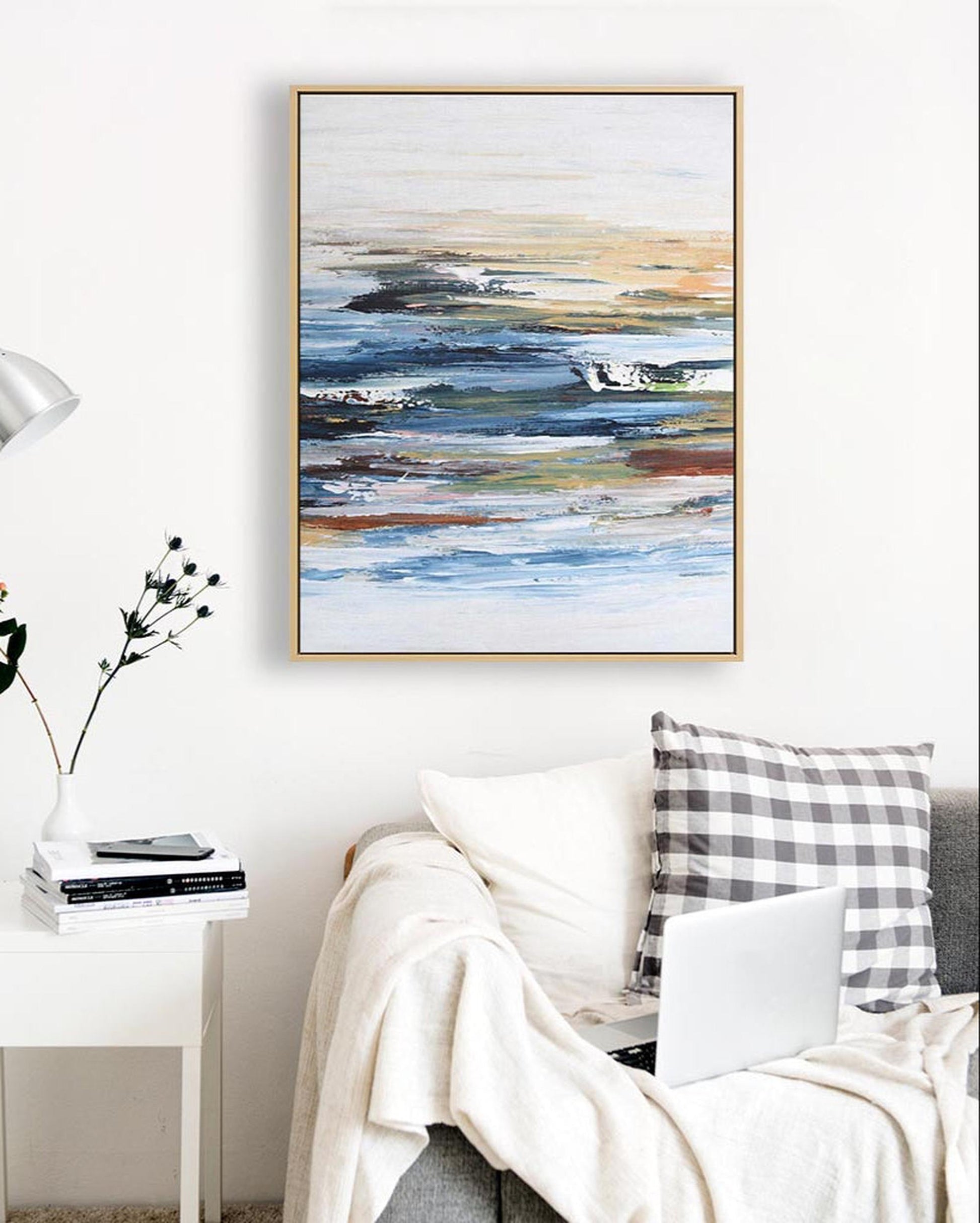 Abstract painting on a wall above a sofa with pillows and a laptop.