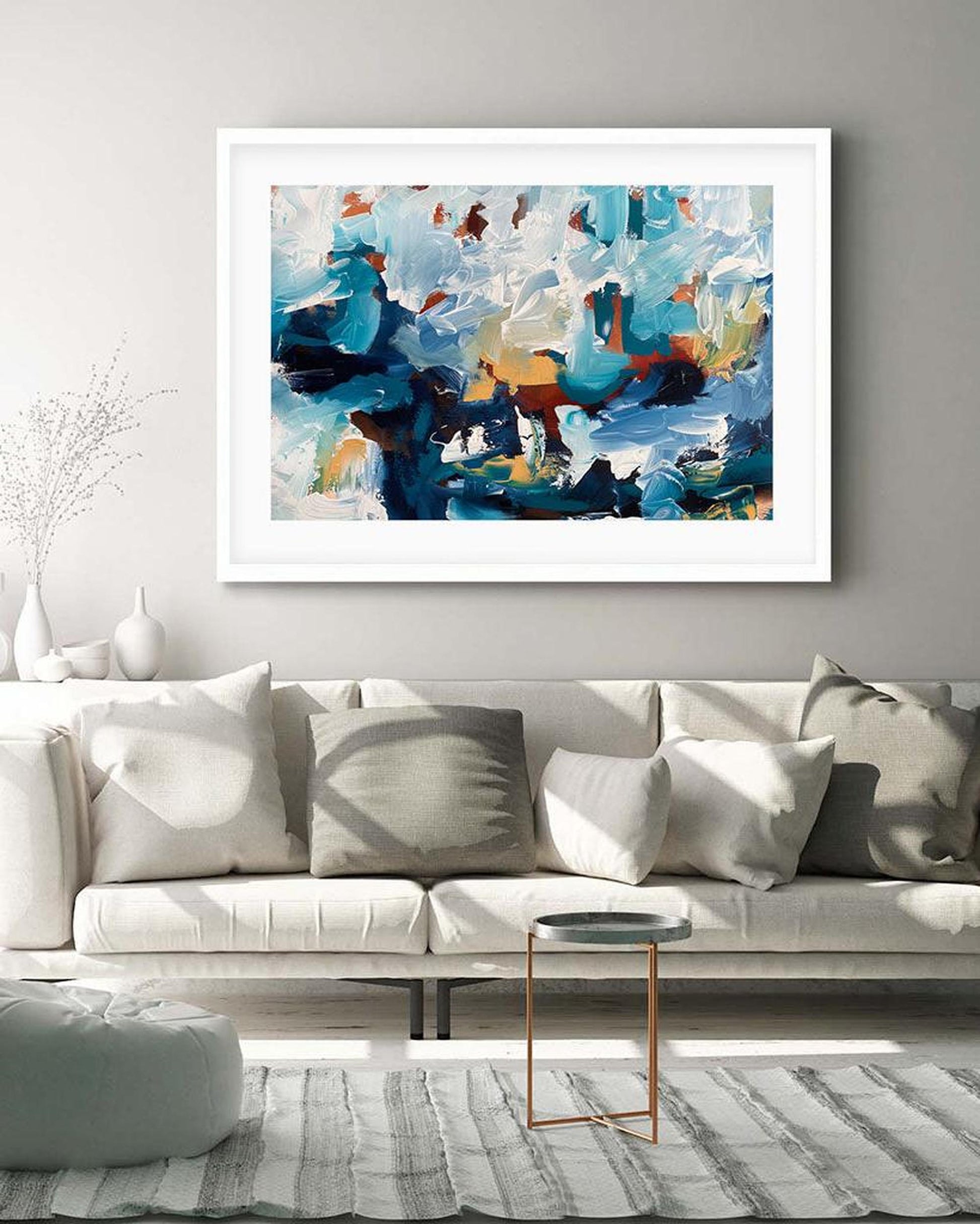 Abstract painting in a white frame above a light gray sofa in a living room.