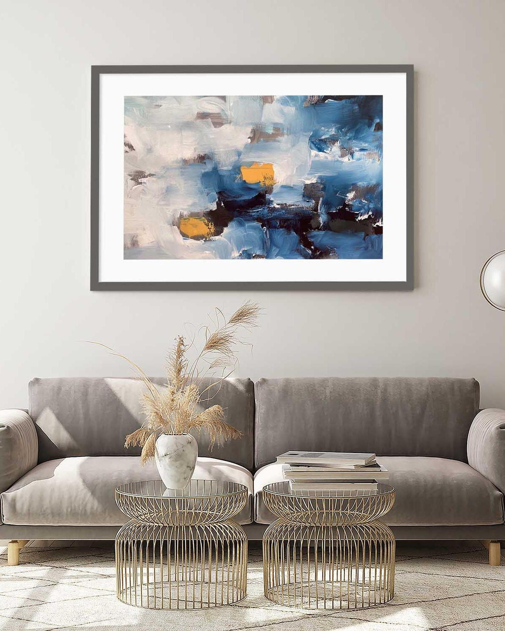 Framed abstract art piece on a wall above a gray sofa with decorative elements.