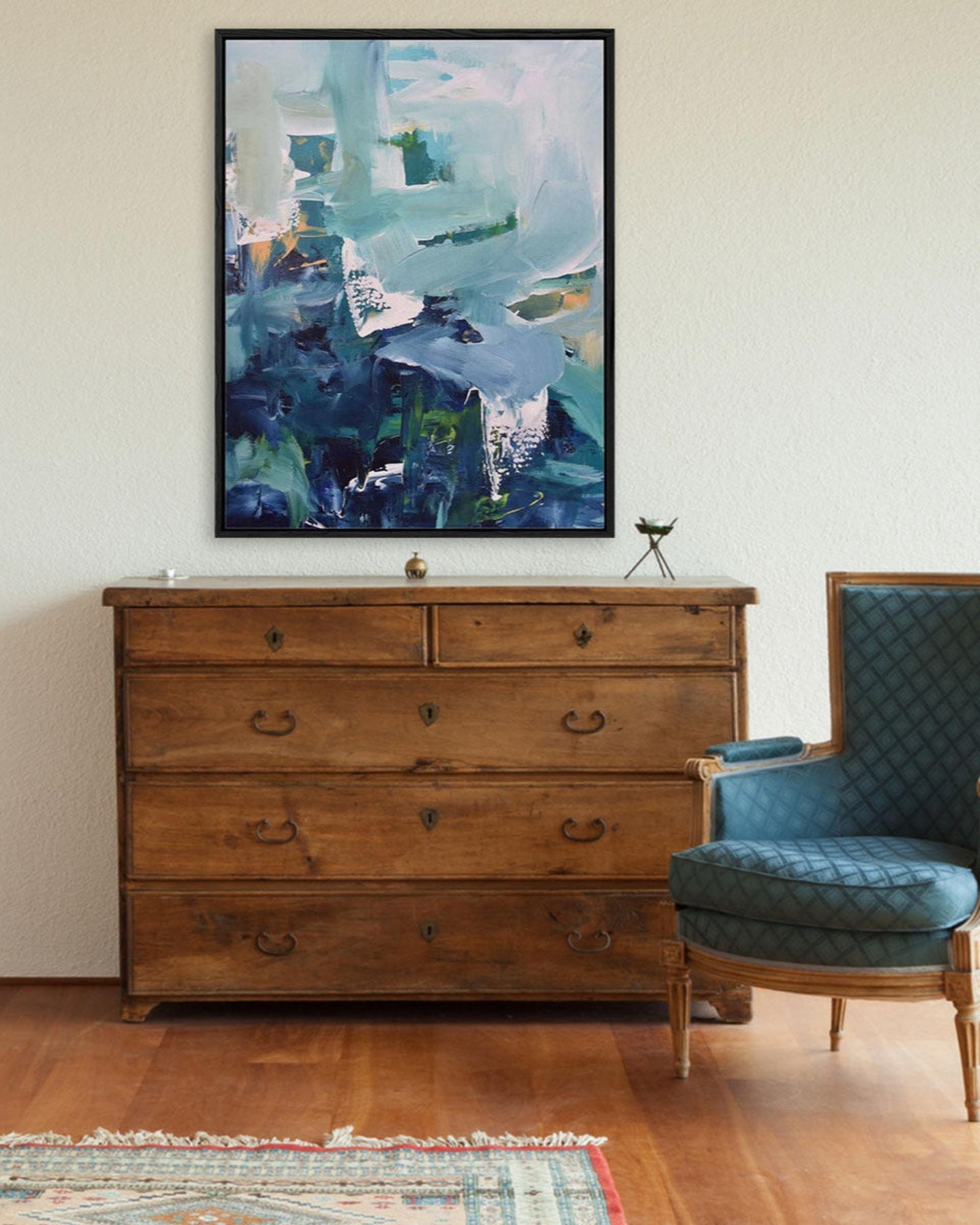 Wooden dresser with abstract painting and blue armchair in a room.