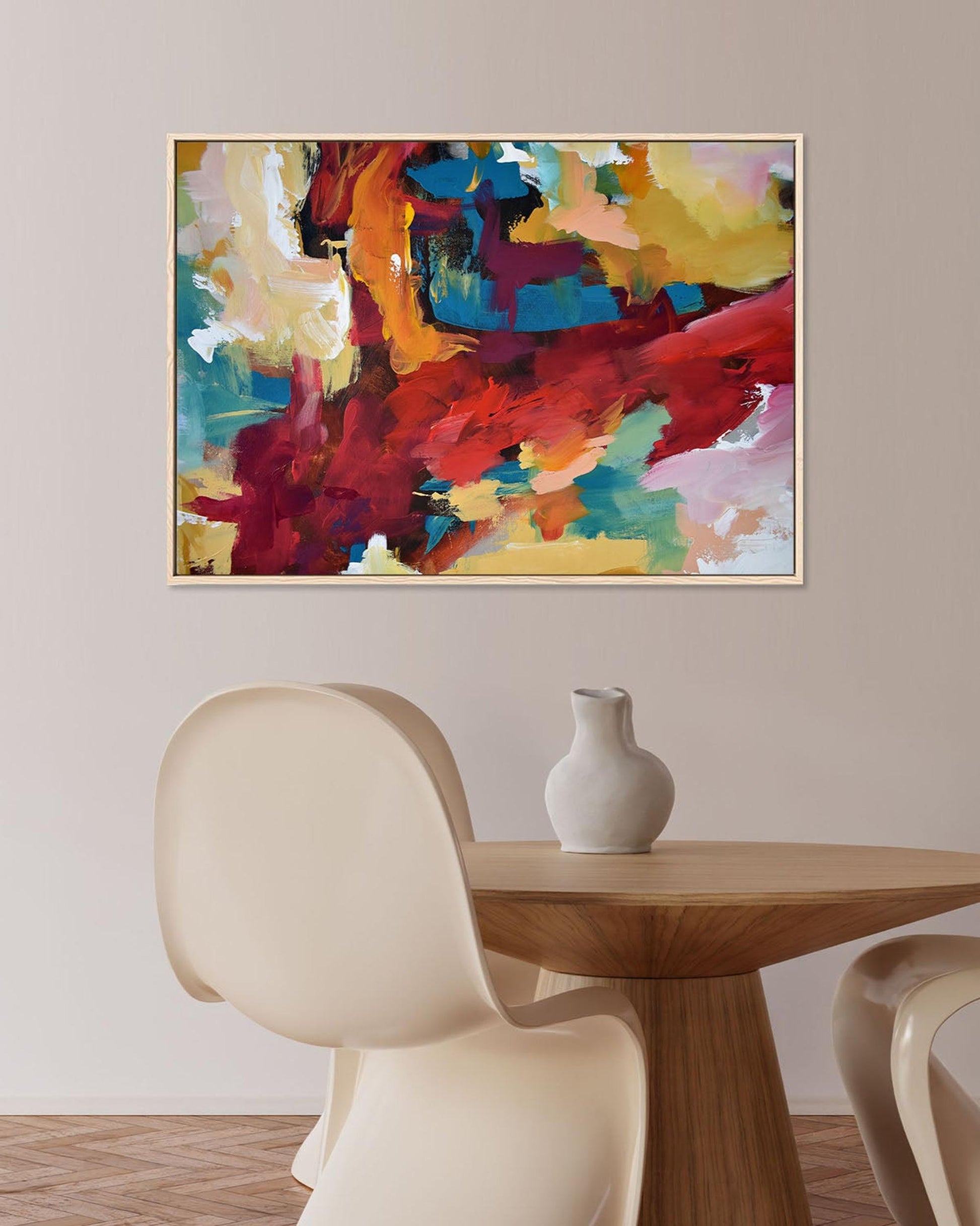 Colorful abstract painting on a wall above a wooden table with a vase and chairs.
