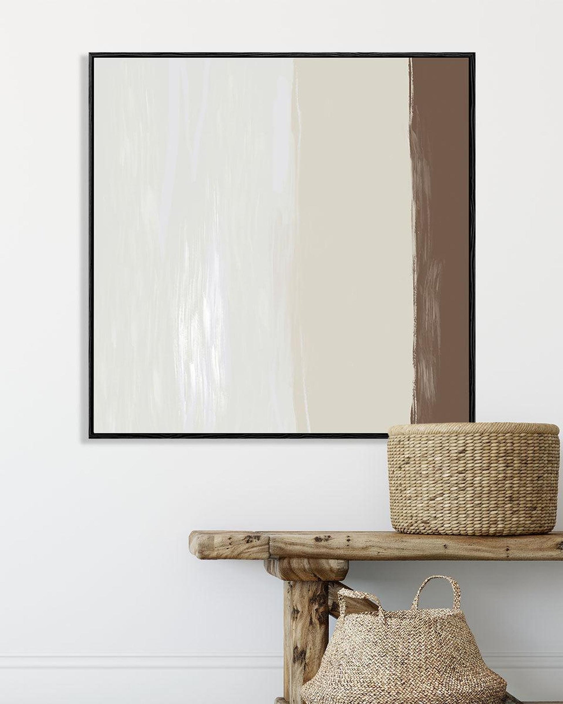 Abstract art piece on a white wall with a wooden console table and woven basket.