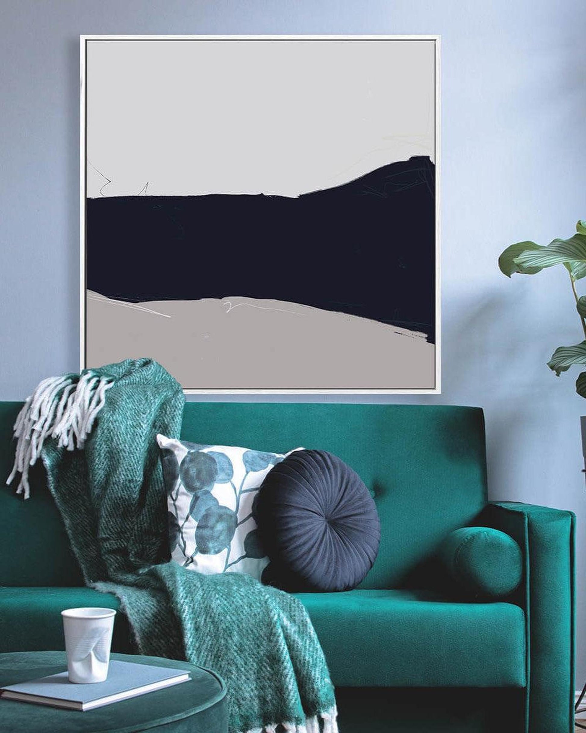Teal sofa with decorative pillows and a green blanket, framed abstract art on the wall.