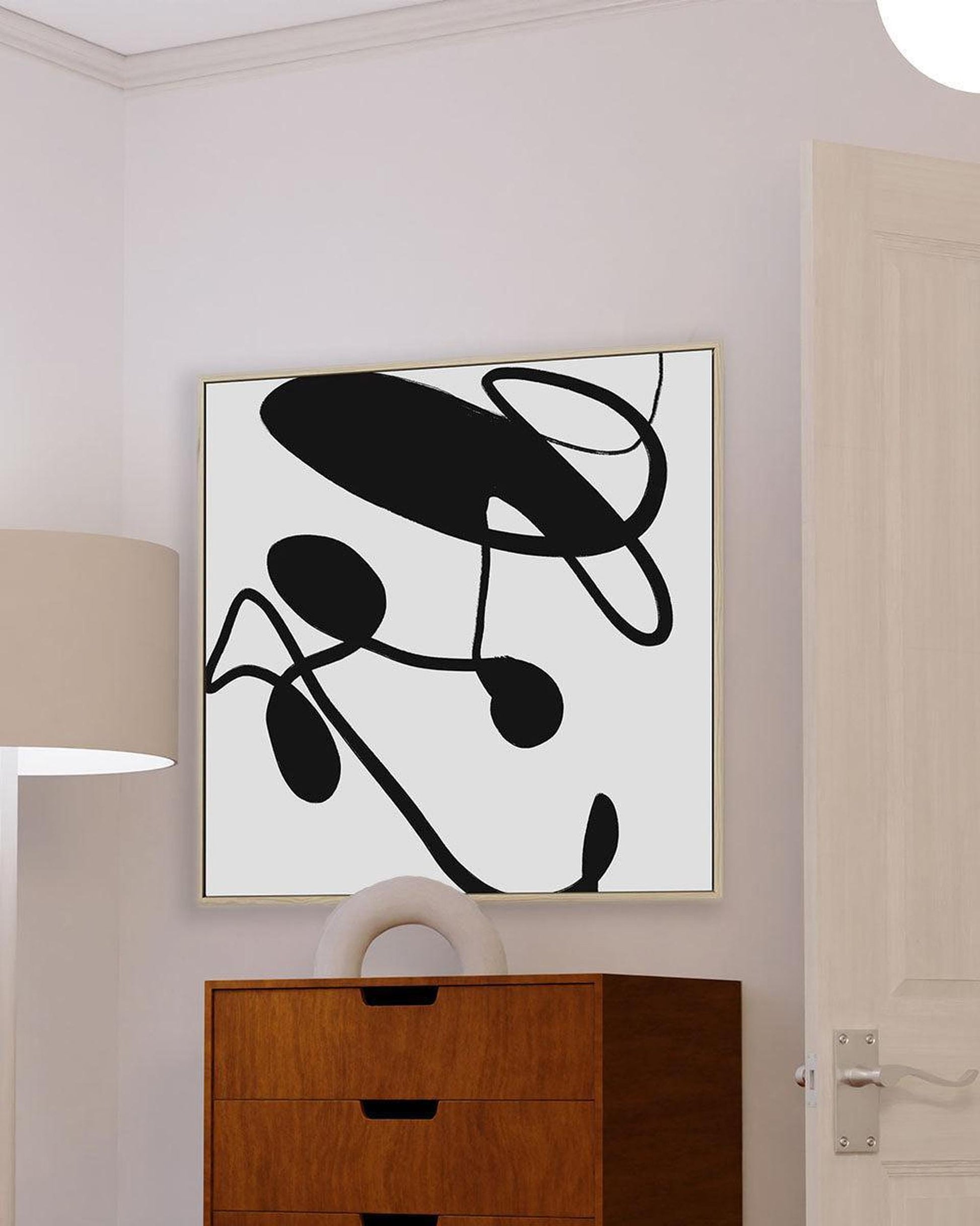 Abstract black and white artwork on a wall above a wooden cabinet.