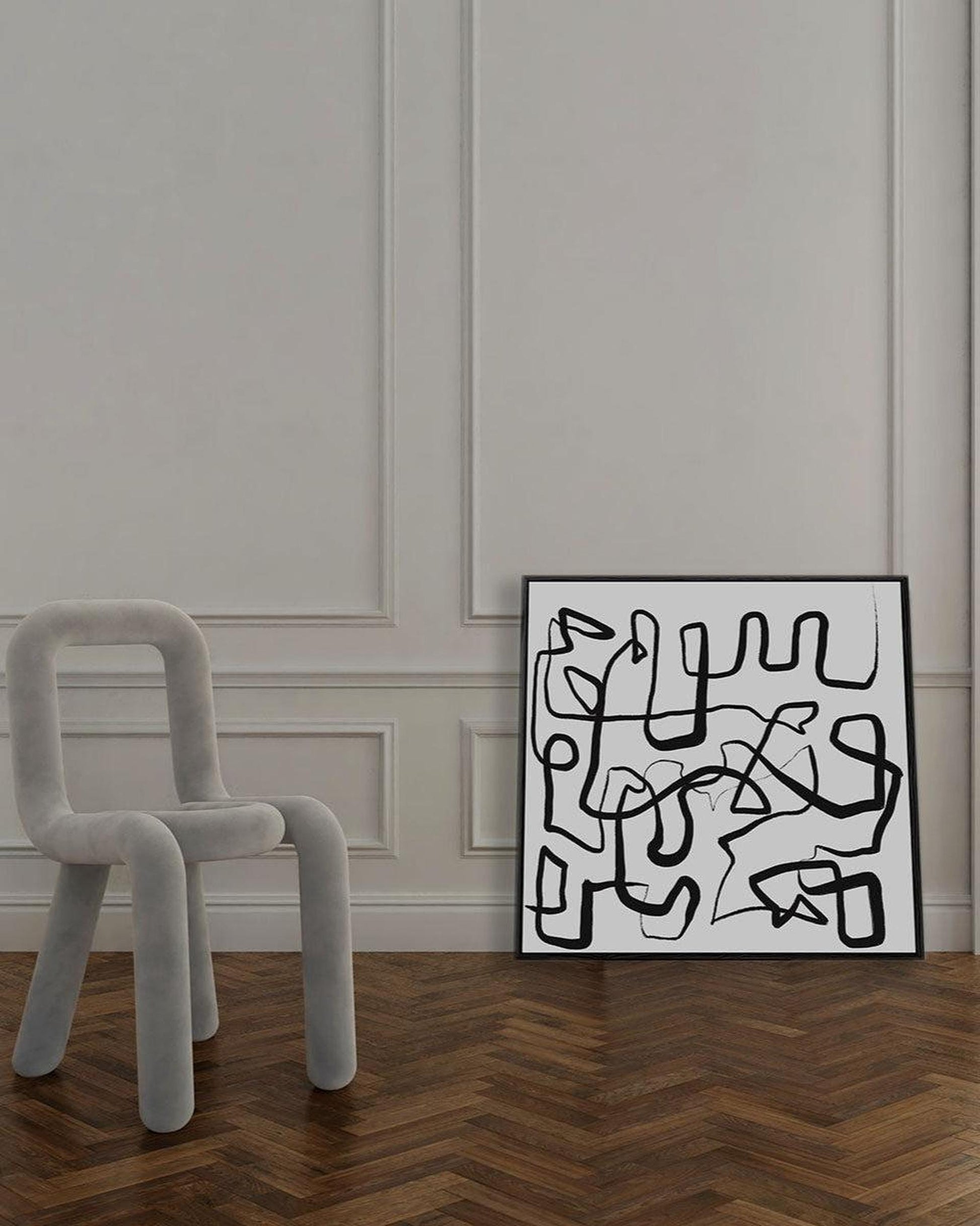Abstract artwork on a wall next to a modern chair in a room with wooden flooring.