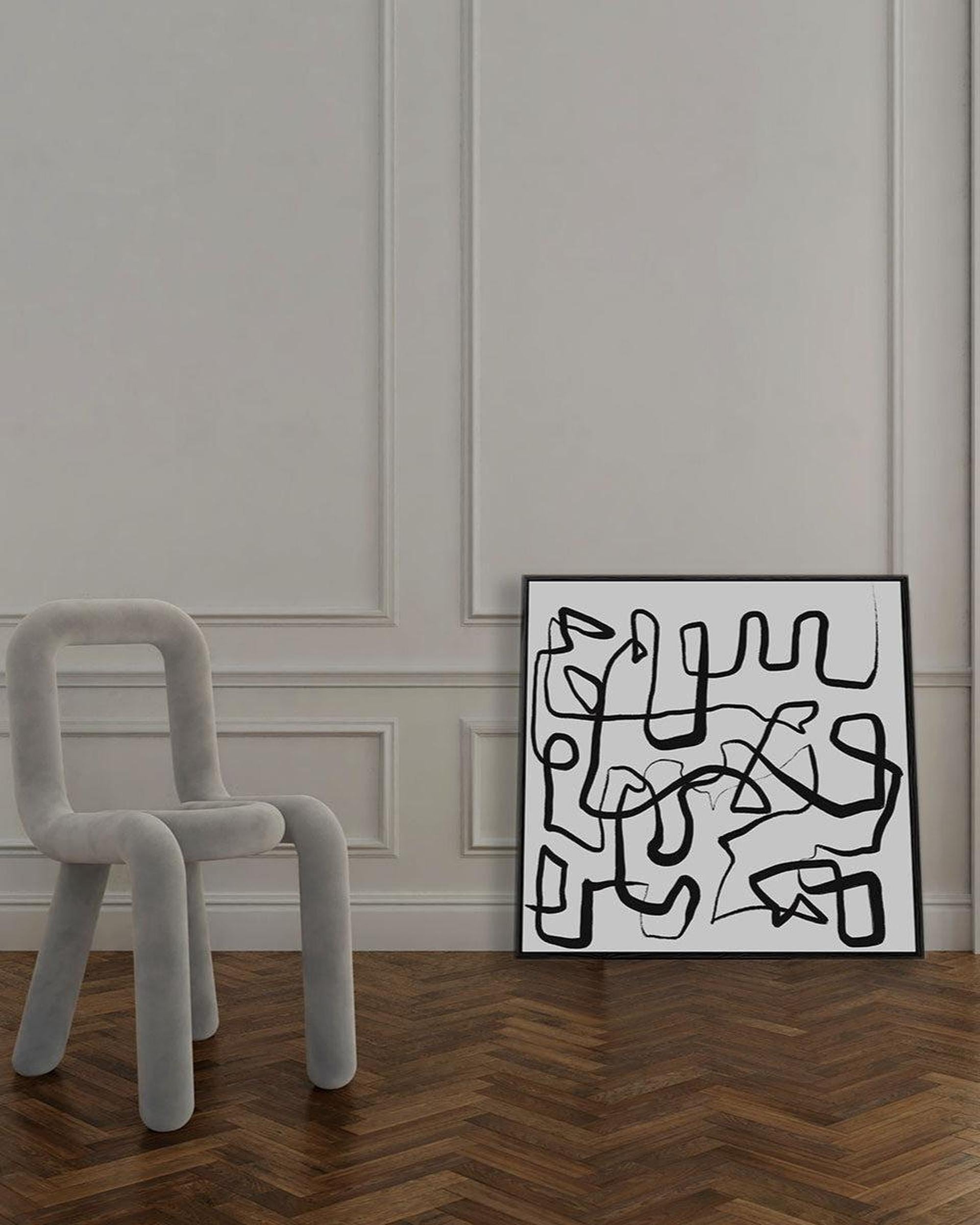 Abstract artwork on a wall next to a modern chair in a room with wooden flooring.