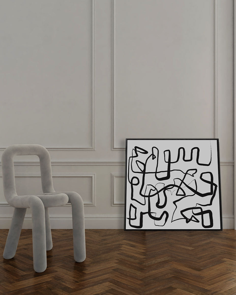 Abstract artwork on a wall next to a modern chair in a room with wooden flooring.
