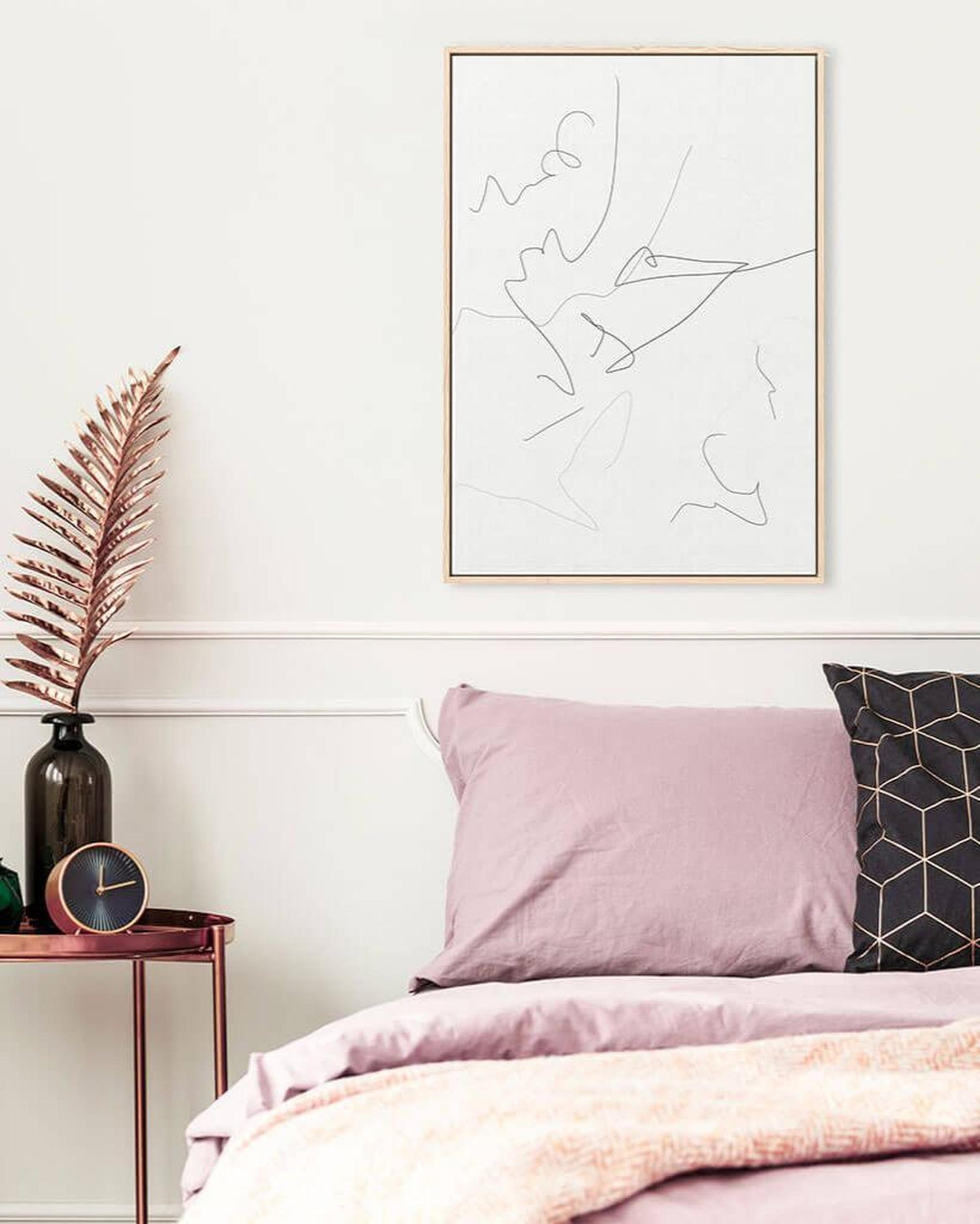 Neatly made bed with pink bedding and pillows, framed abstract art on the wall.