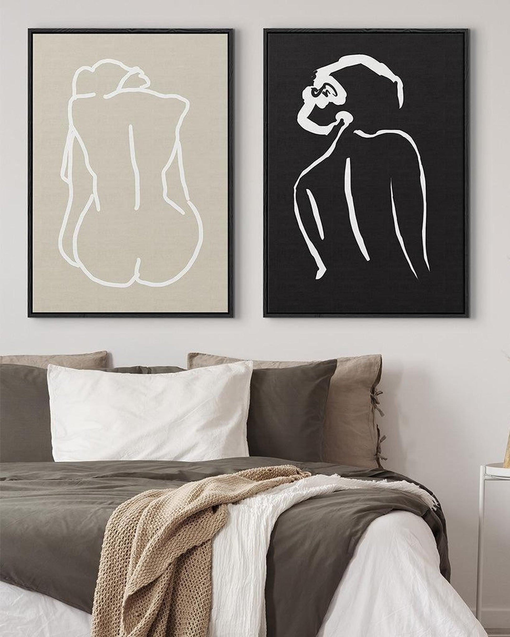 Two framed line art prints of a nude figure and a monkey on a wall above a bed.