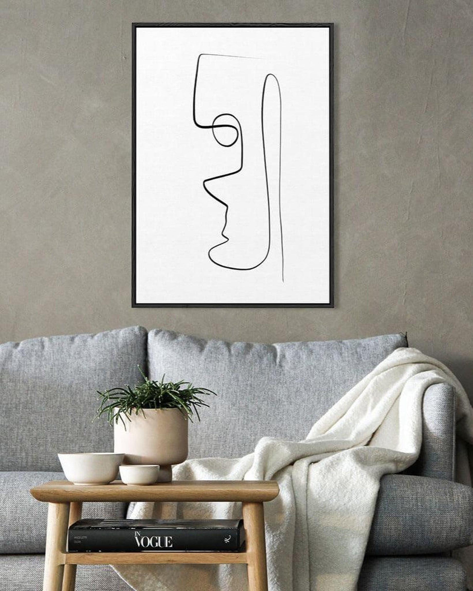 Abstract line art of a face on a wall above a gray sofa with a wooden side table.