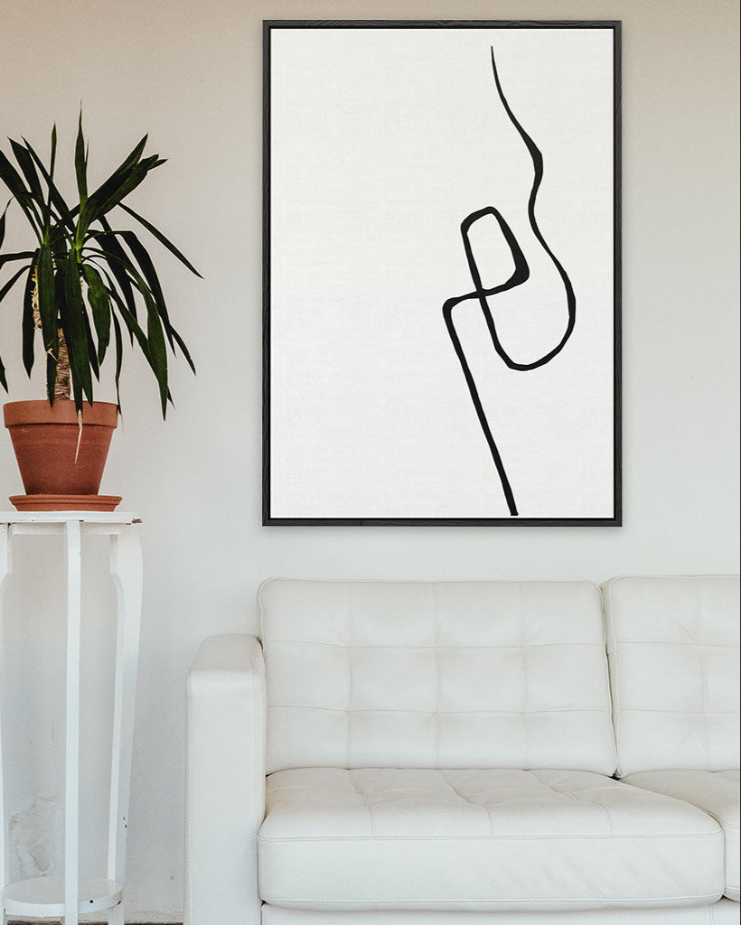Abstract line art in a black frame on a white wall above a white sofa with a plant beside it.