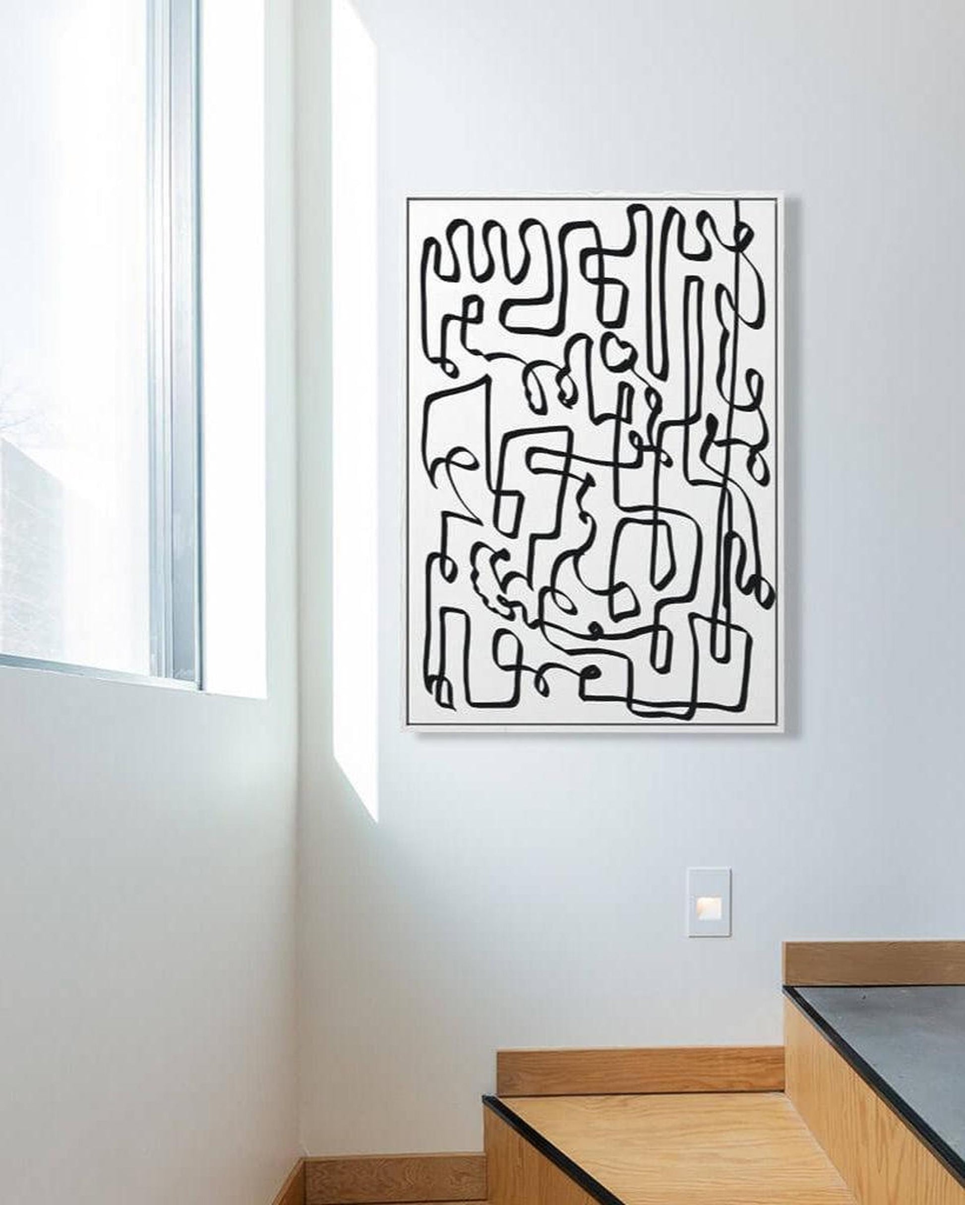 Abstract black and white artwork on a white wall with a window in the background.