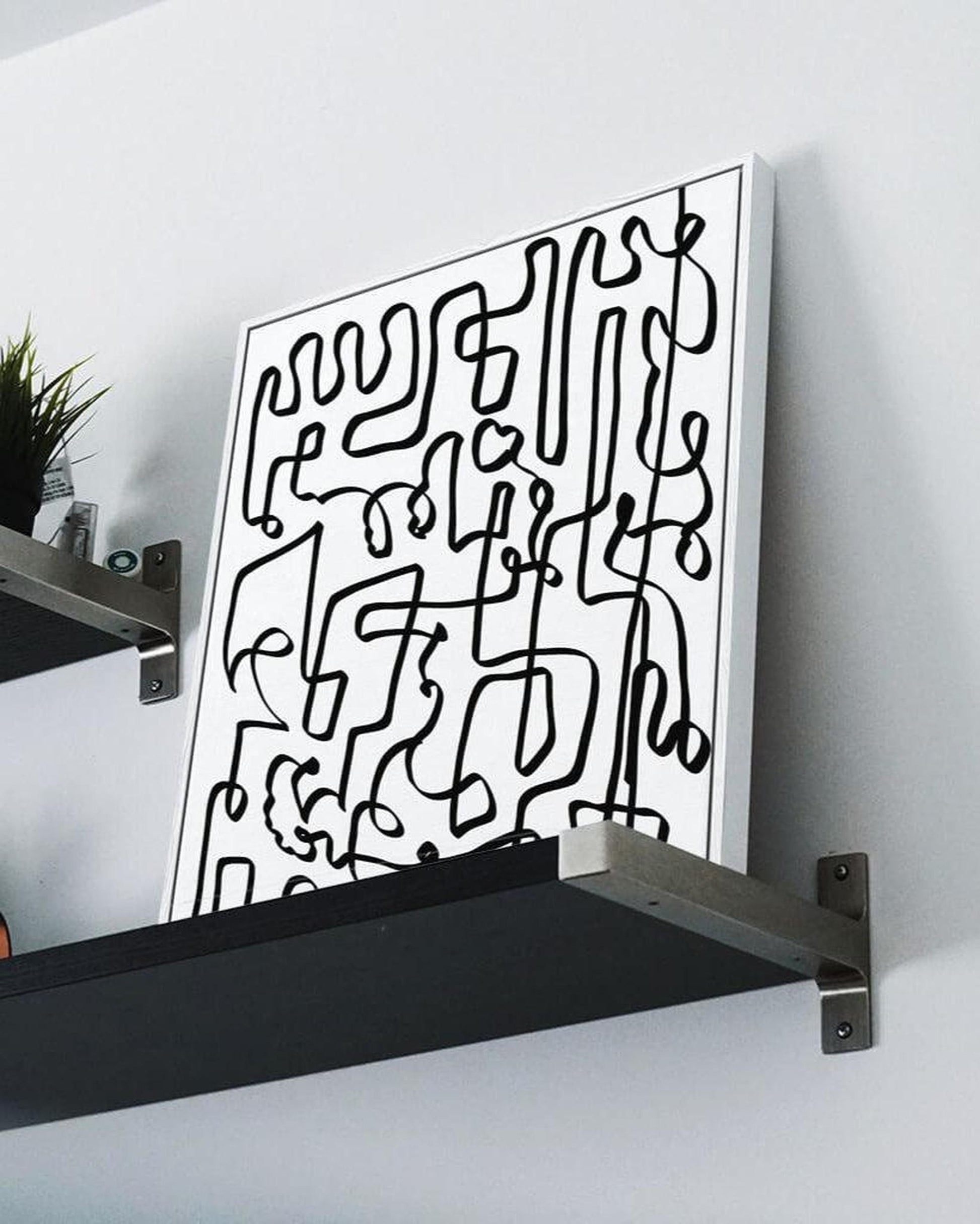 Abstract black line art on a white background displayed on a wall with a black shelf.