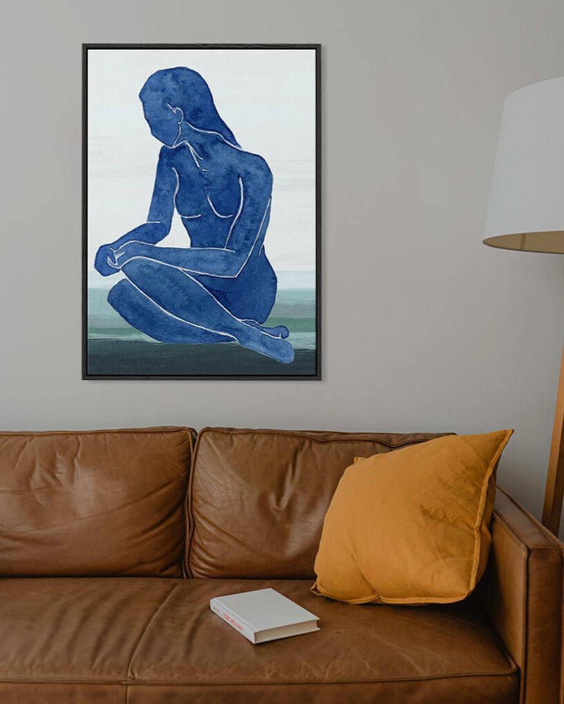 Framed artwork of a blue silhouette on a wall above a brown sofa with a yellow pillow.