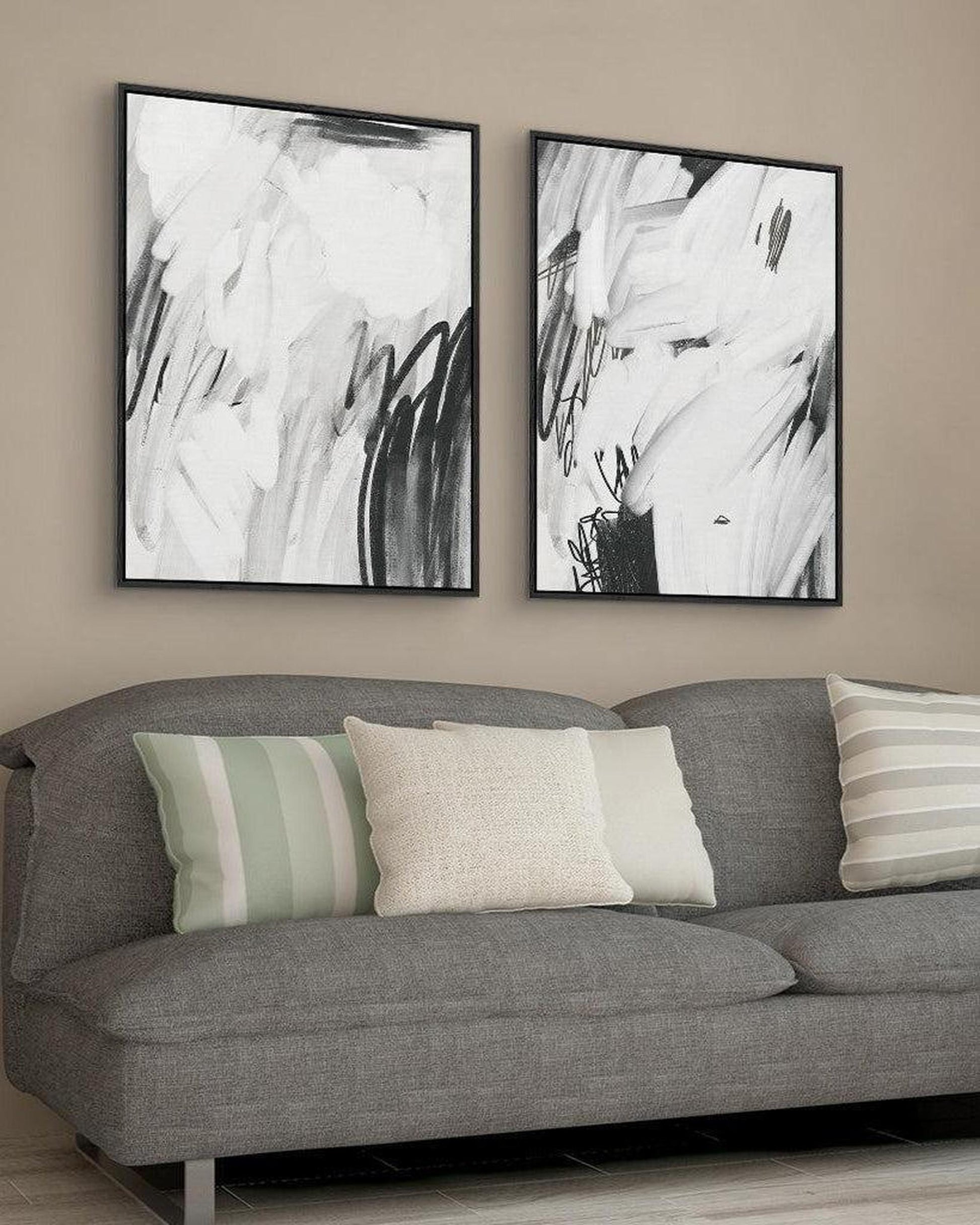 Two abstract black and white paintings above a gray sofa with colorful cushions.