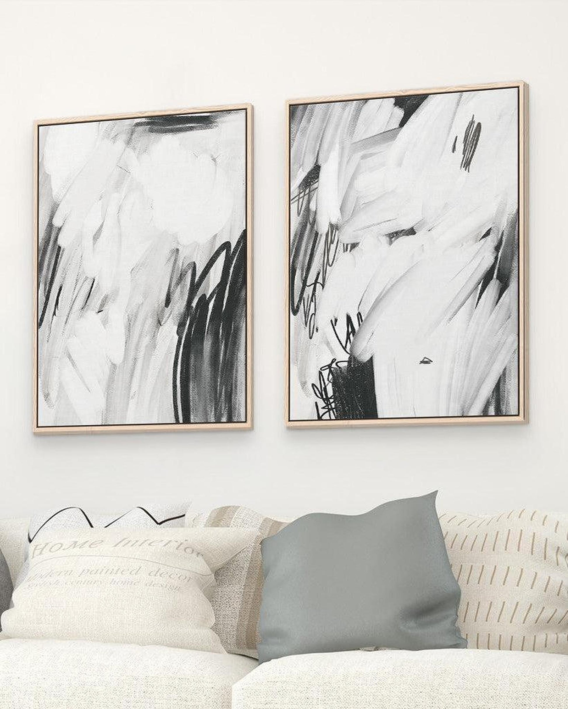 Two abstract black and white paintings on a wall above a sofa.