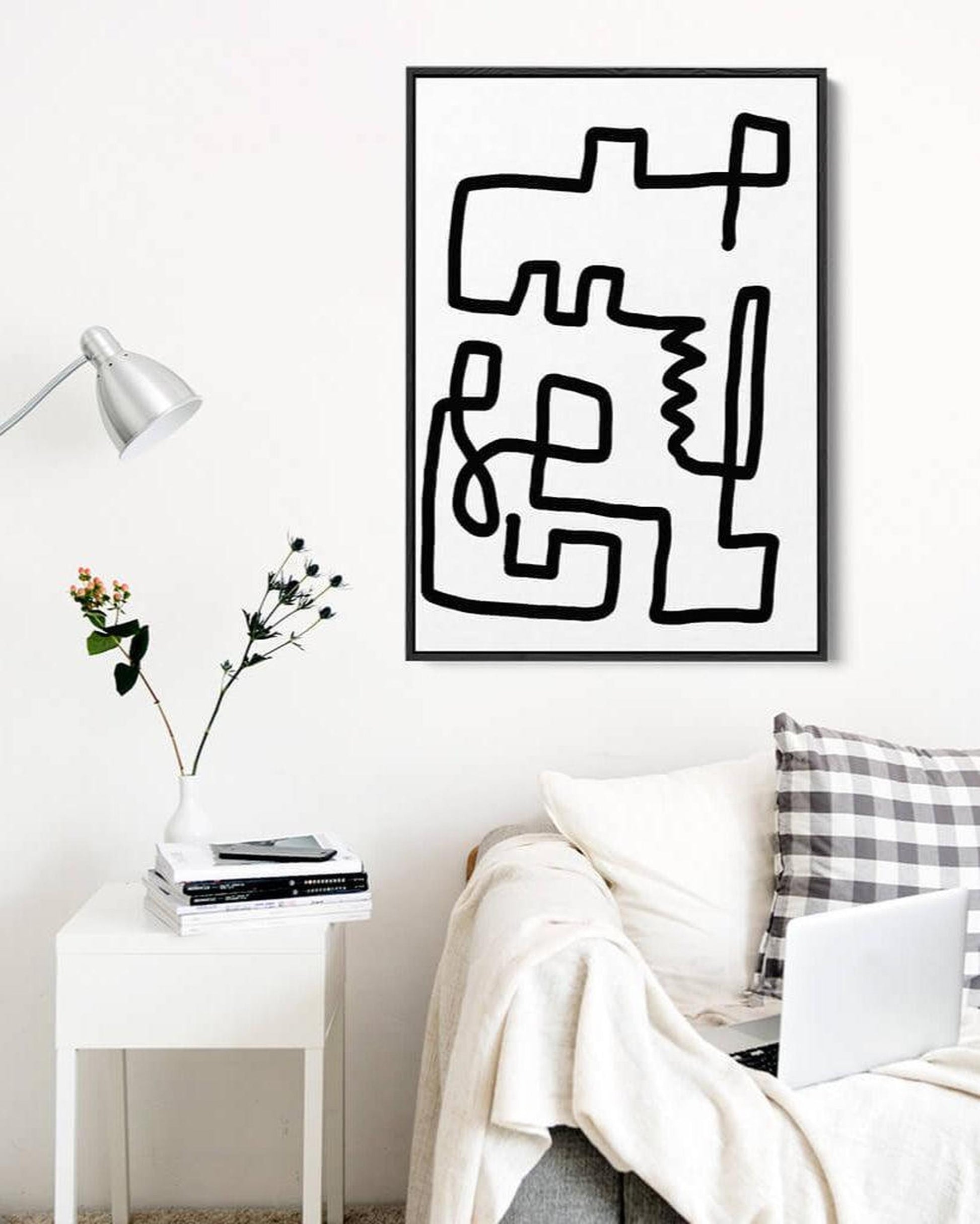 Abstract black and white artwork on a wall above a sofa with a side table and lamp.
