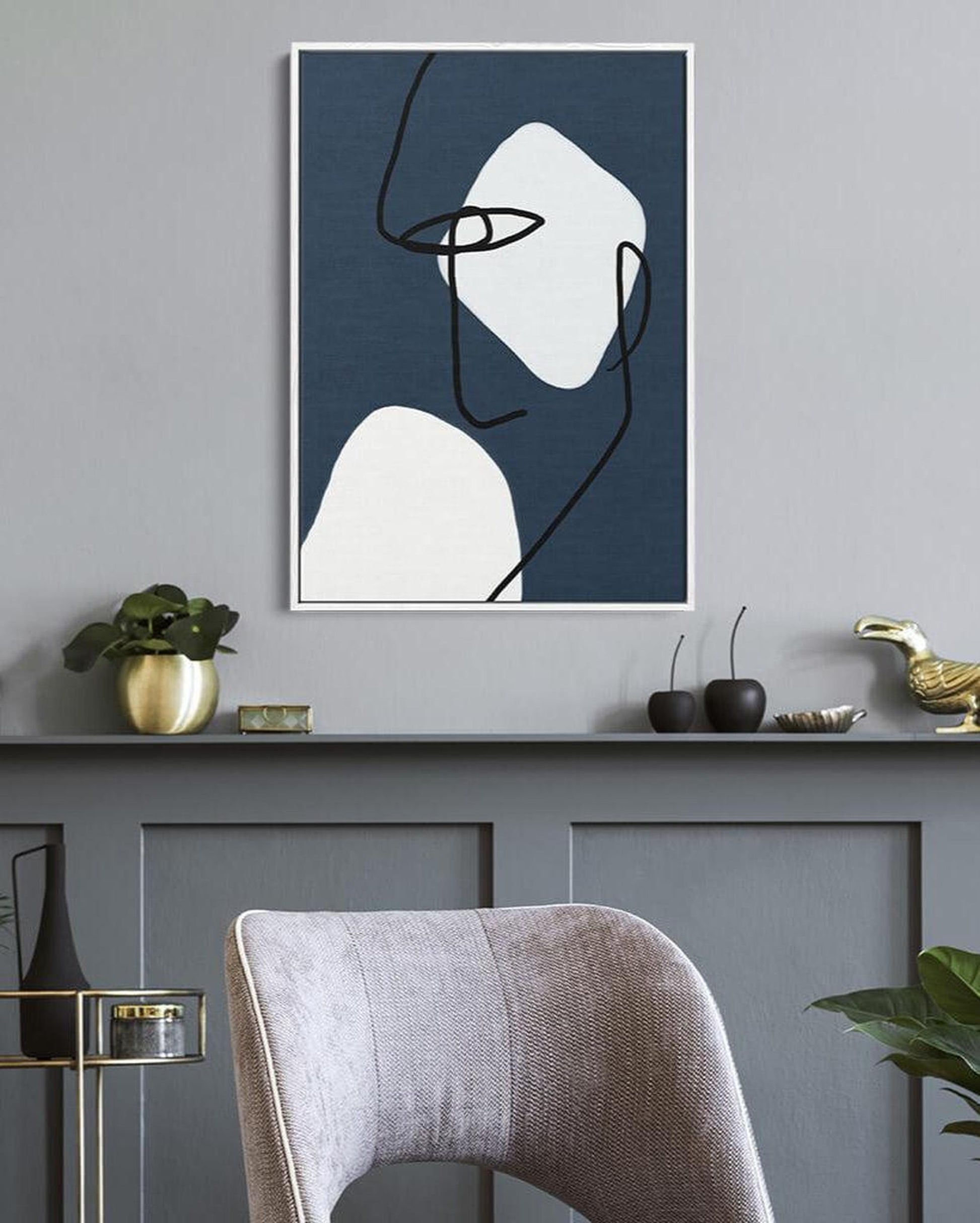 Abstract line art print on a wall above a gray cabinet with decorative items.