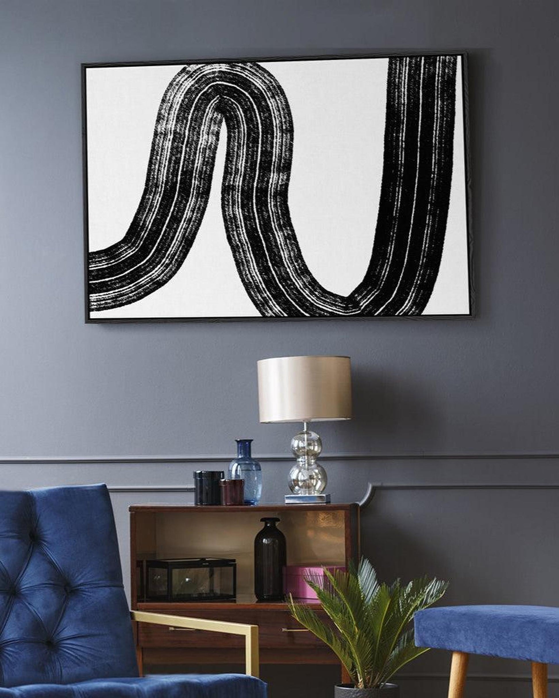 Abstract black and white artwork on a gray wall above a wooden side table with decorative items.