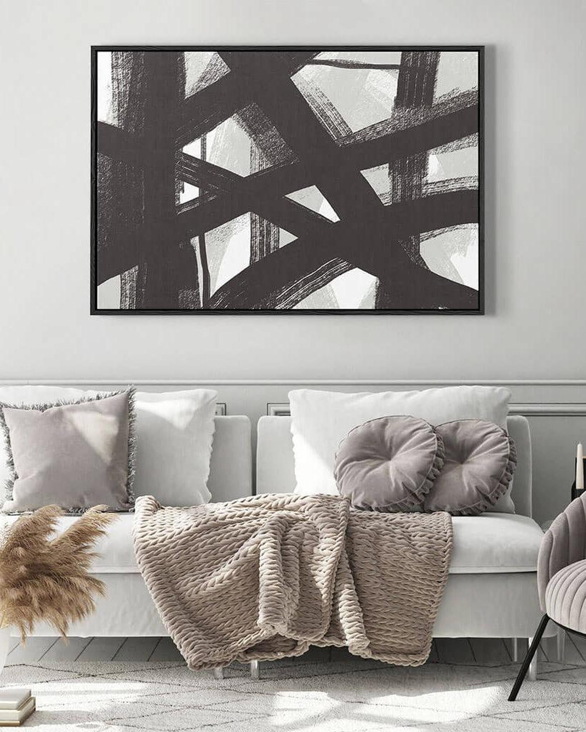 Abstract black and white painting above a sofa with decorative pillows and a blanket.