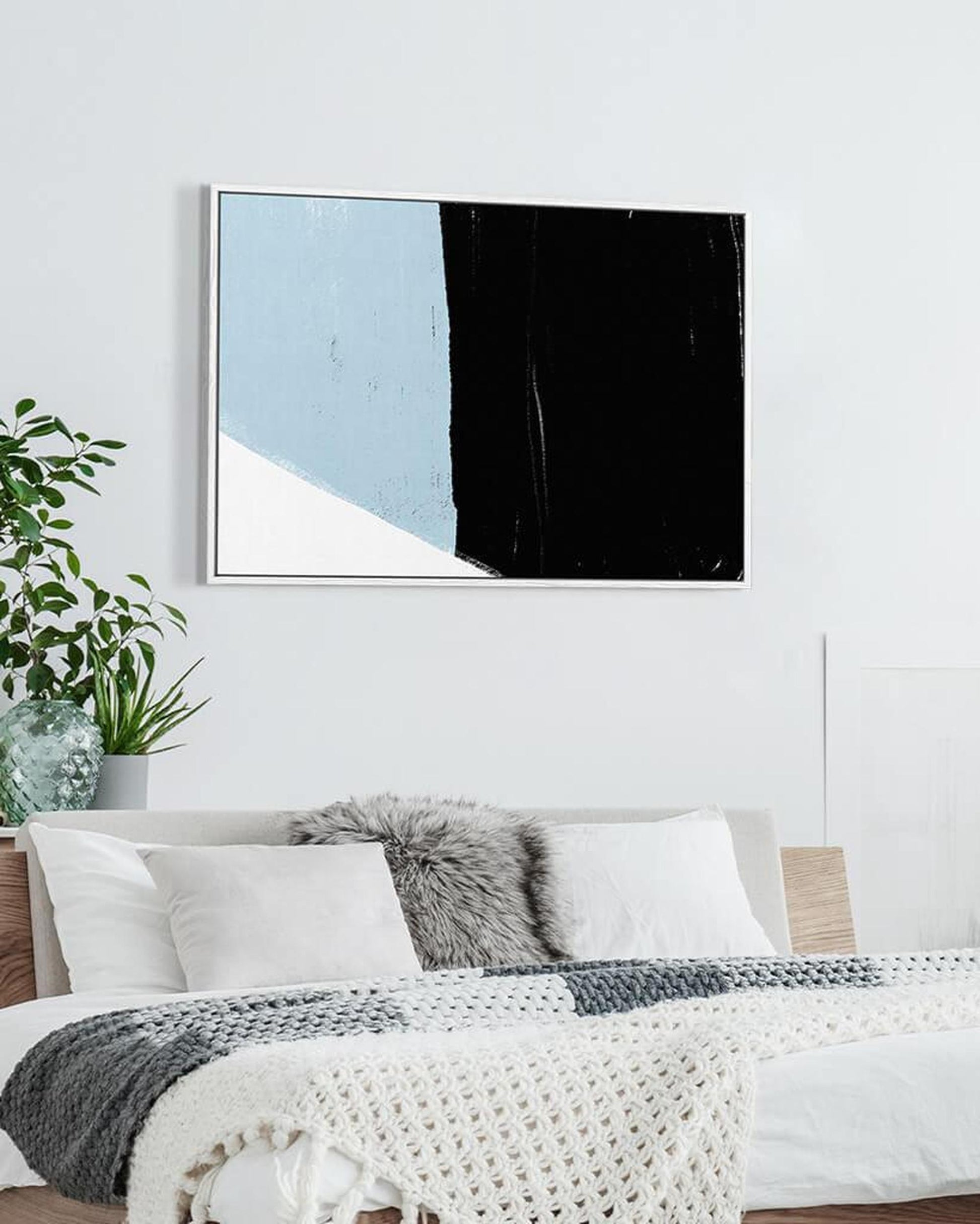 Abstract art piece with blue, black, and white colors on a wall above a bed.