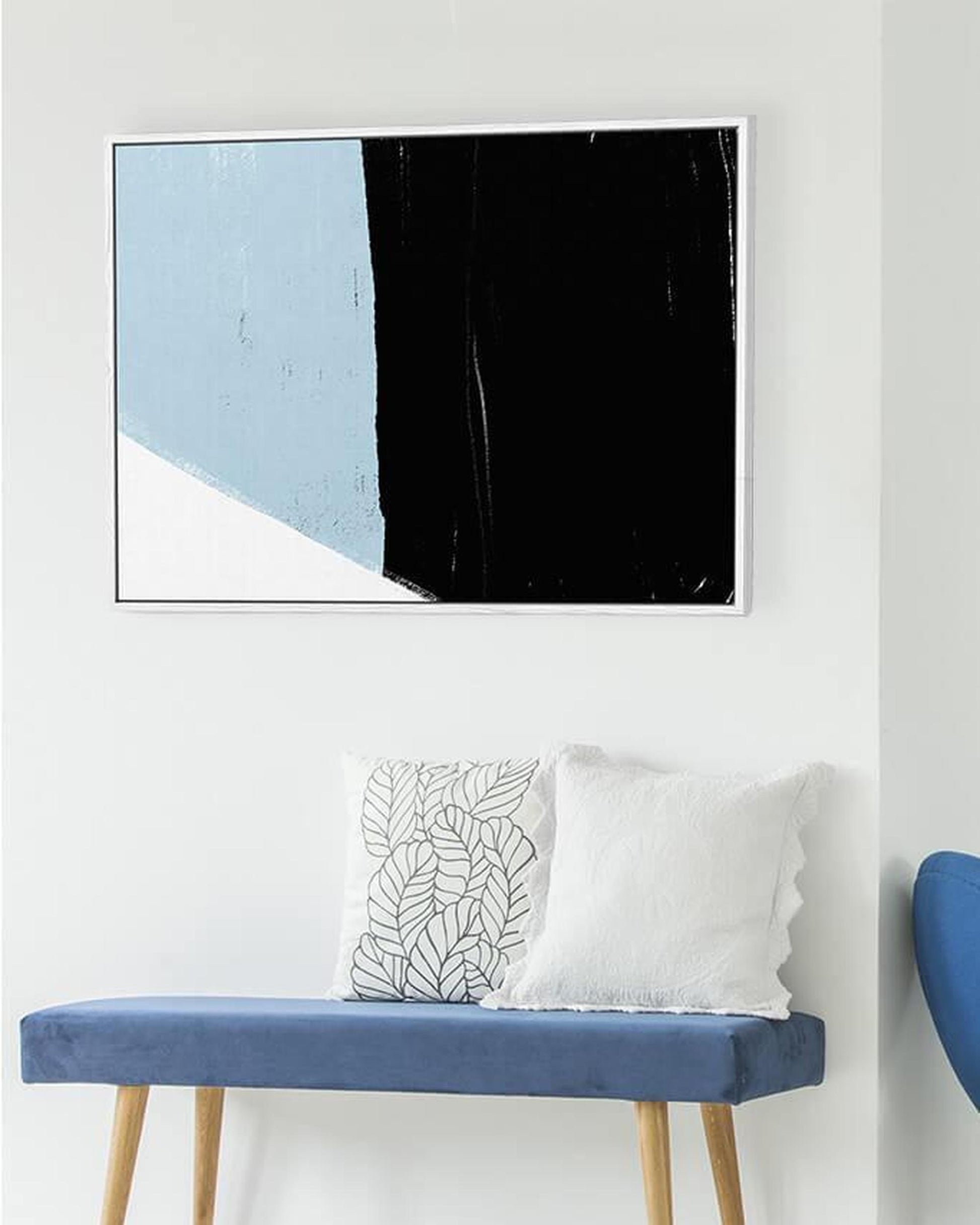 Abstract art piece with blue, black, and white on a white wall above a blue bench.