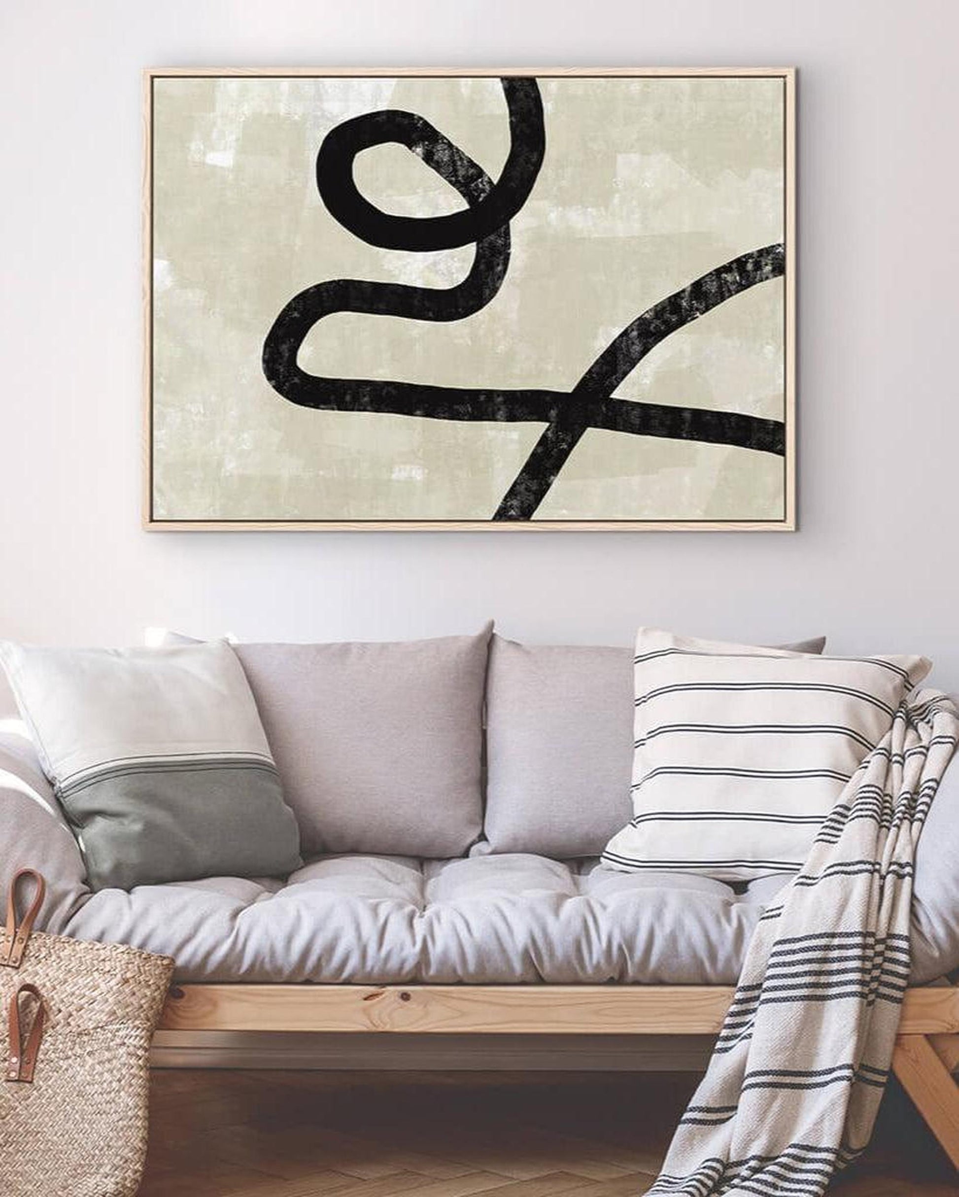 Abstract black line art on a light background above a sofa with decorative pillows and a blanket.